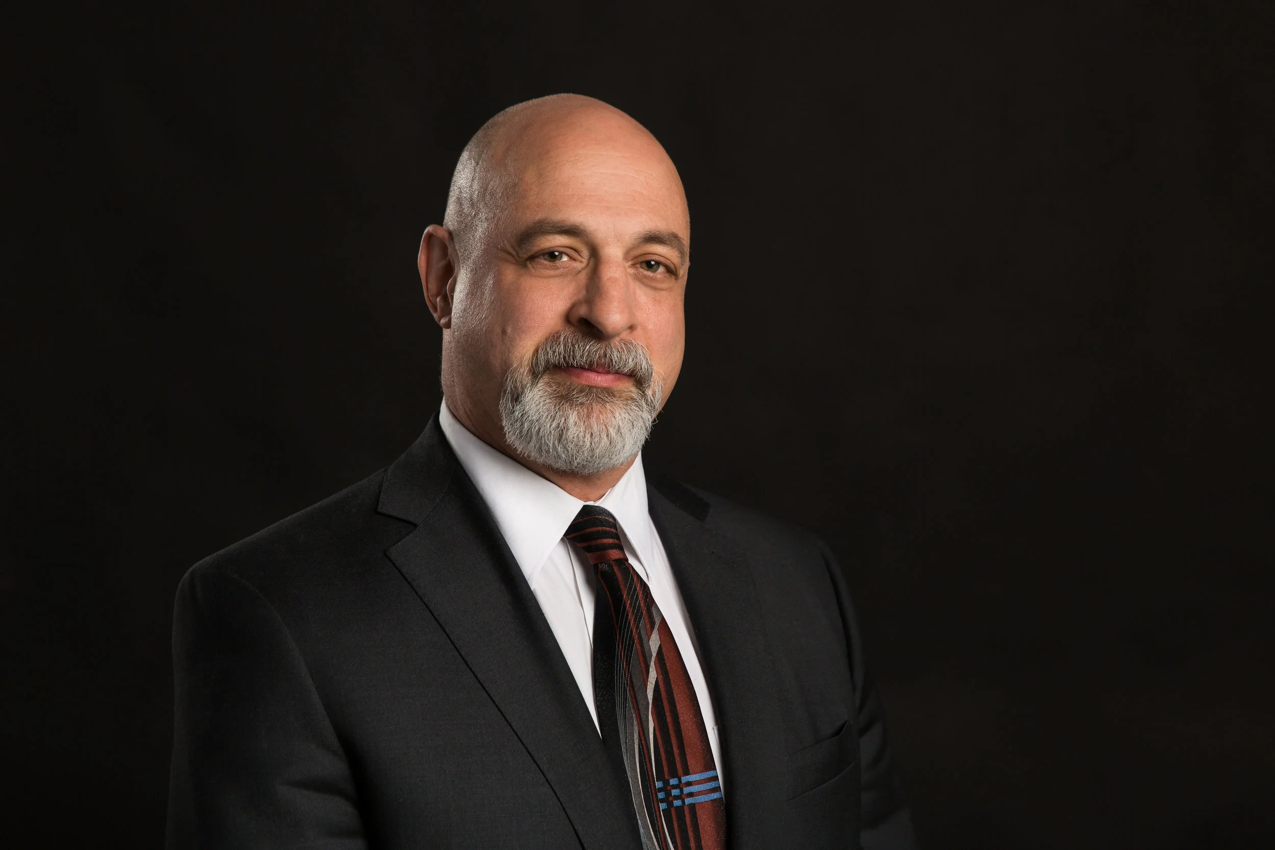 Headshot on a black backdrop of a man in a suit