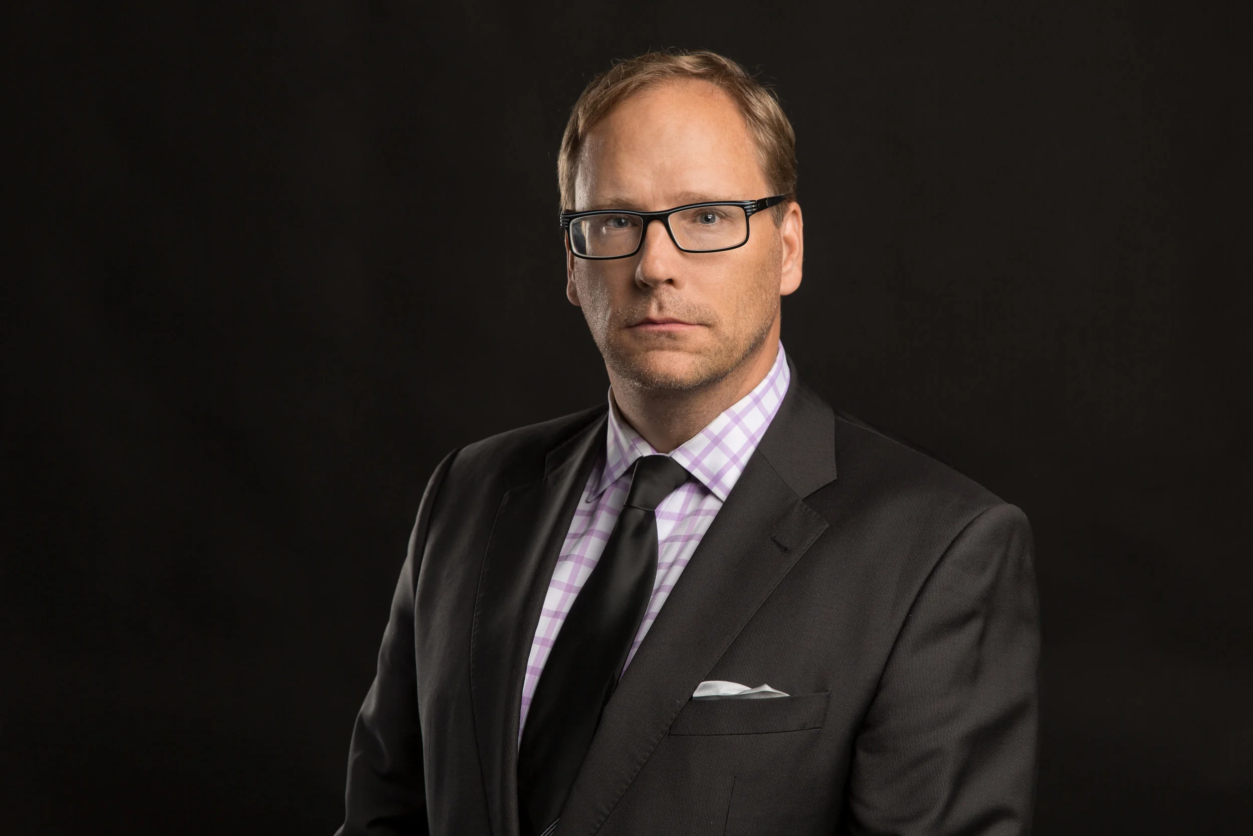 Headshot on a black backdrop of a man in a suit