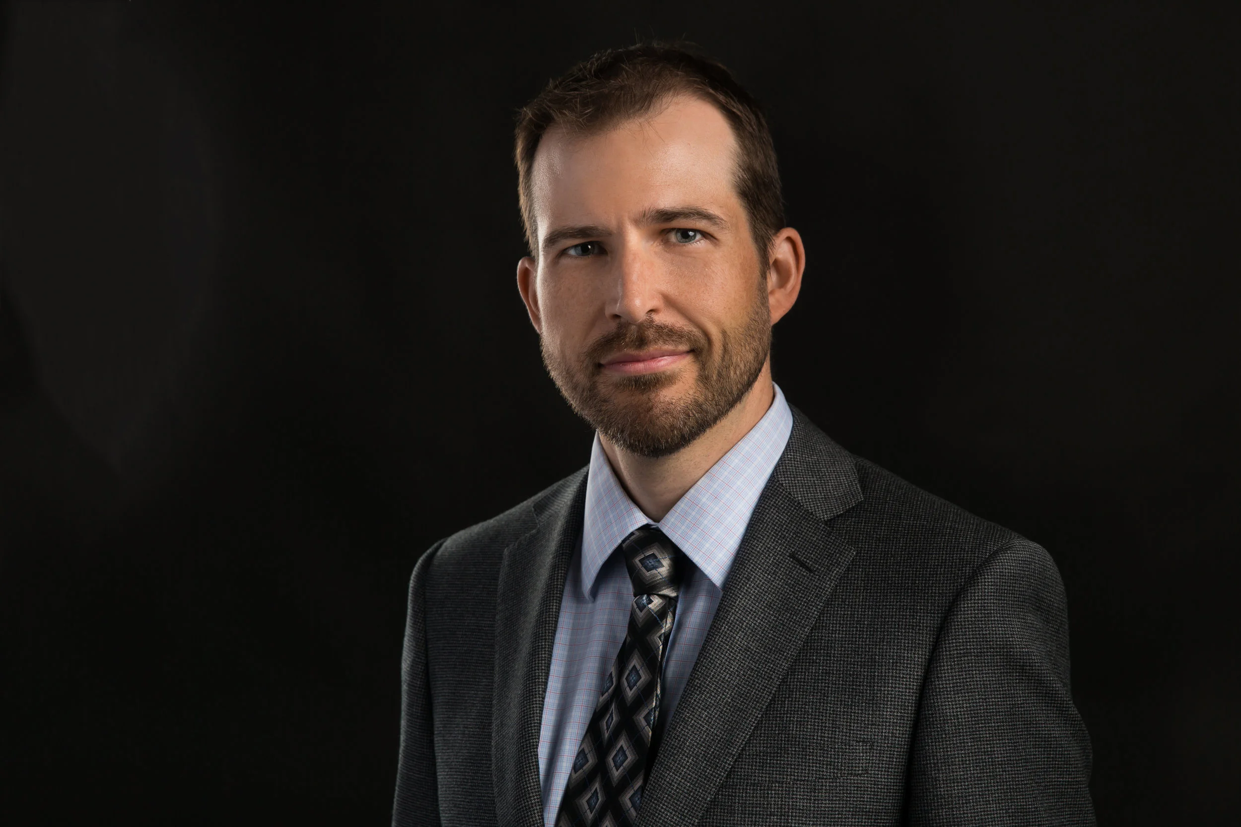 Headshot on a black backdrop of a man in a suit