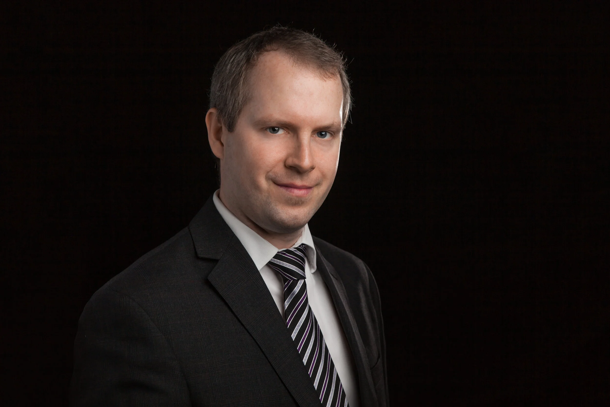 Headshot on a black backdrop of a man in a suit