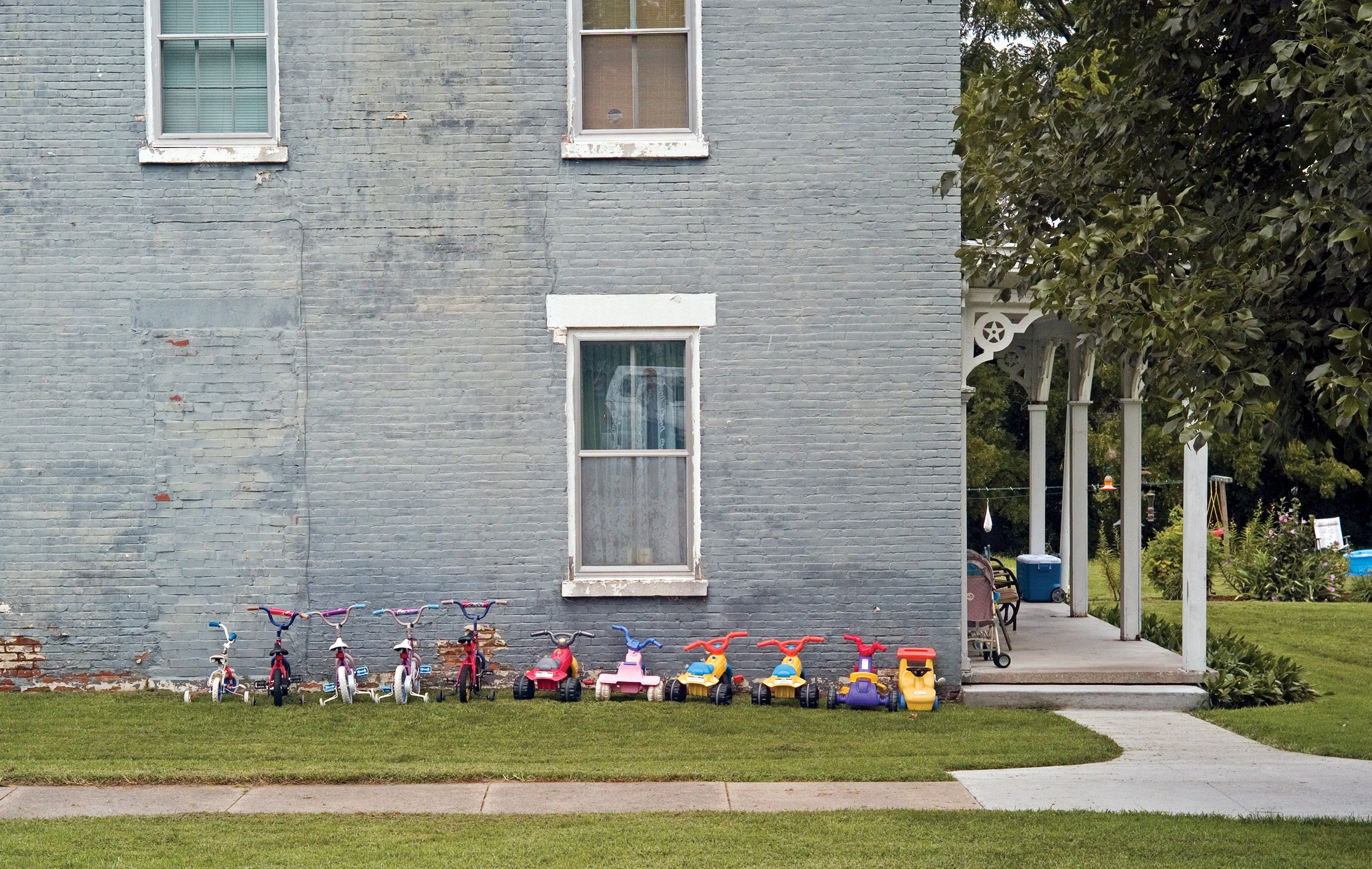  Tricycles lined up in a row outside brick building used as a daycare center. Warsaw, IL. 2009. 