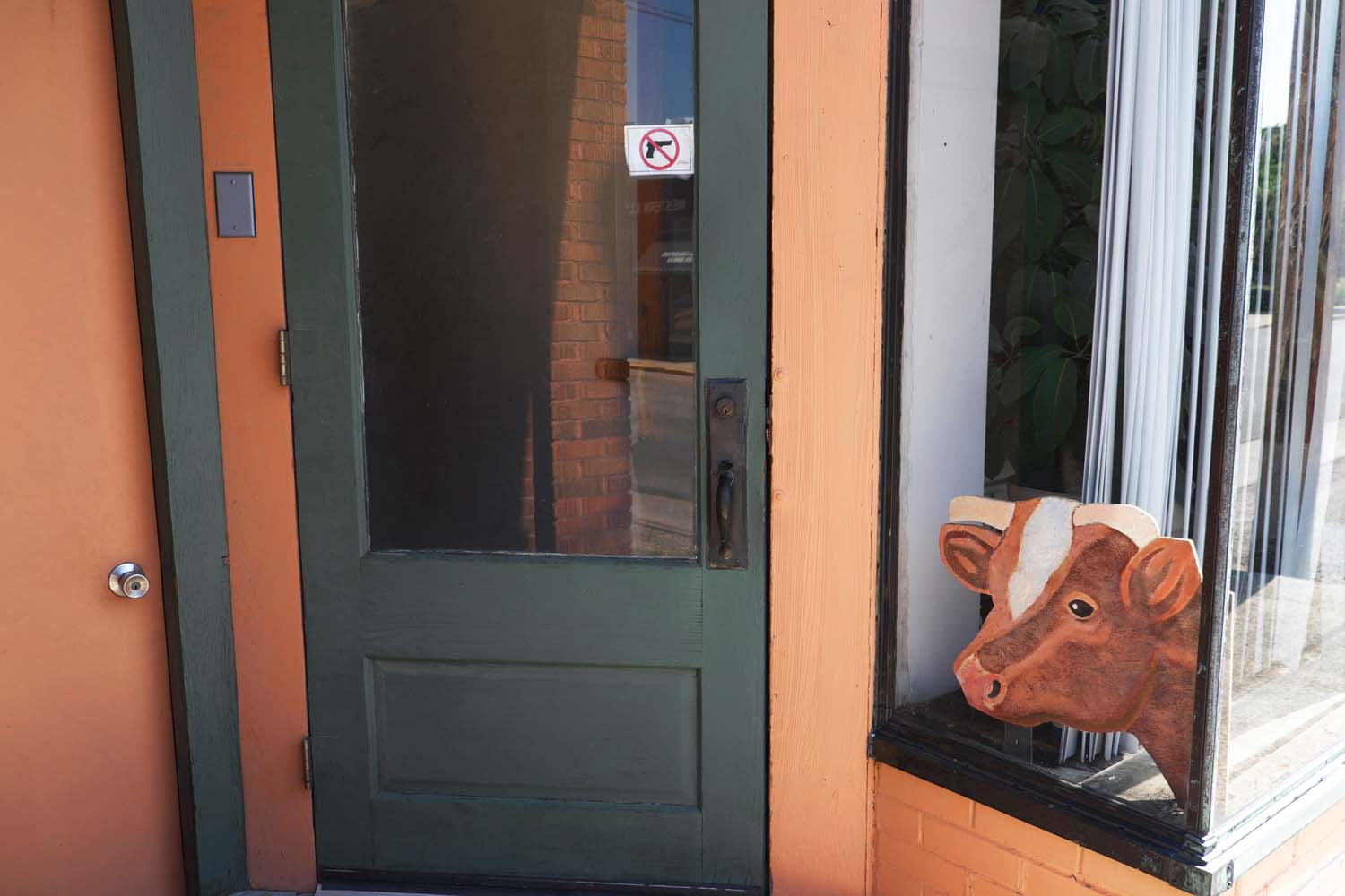  Shop window with a cow sign and a No Guns Allowed decal. Macomb, IL. June, 2016 