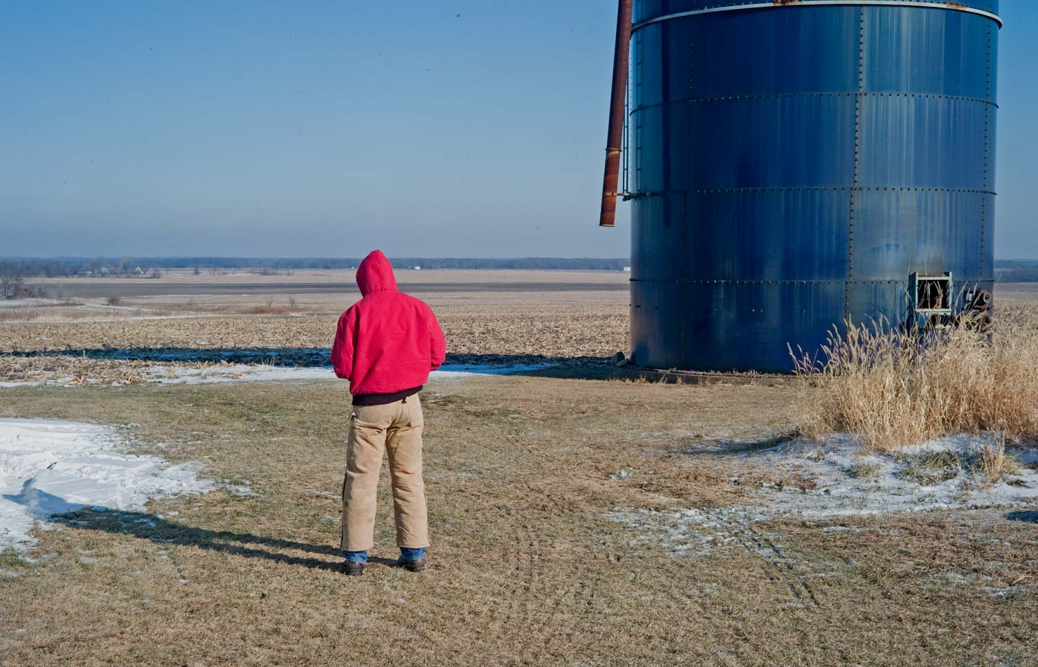  Man standing in an open field next to Blue Harvestore Silo used to store silage used for animal feed. The farm crisis of the early 80s collapsed cattle and dairy farms, hence the nickname Blue Tombstones. Sutter, IL. December, 2010. 