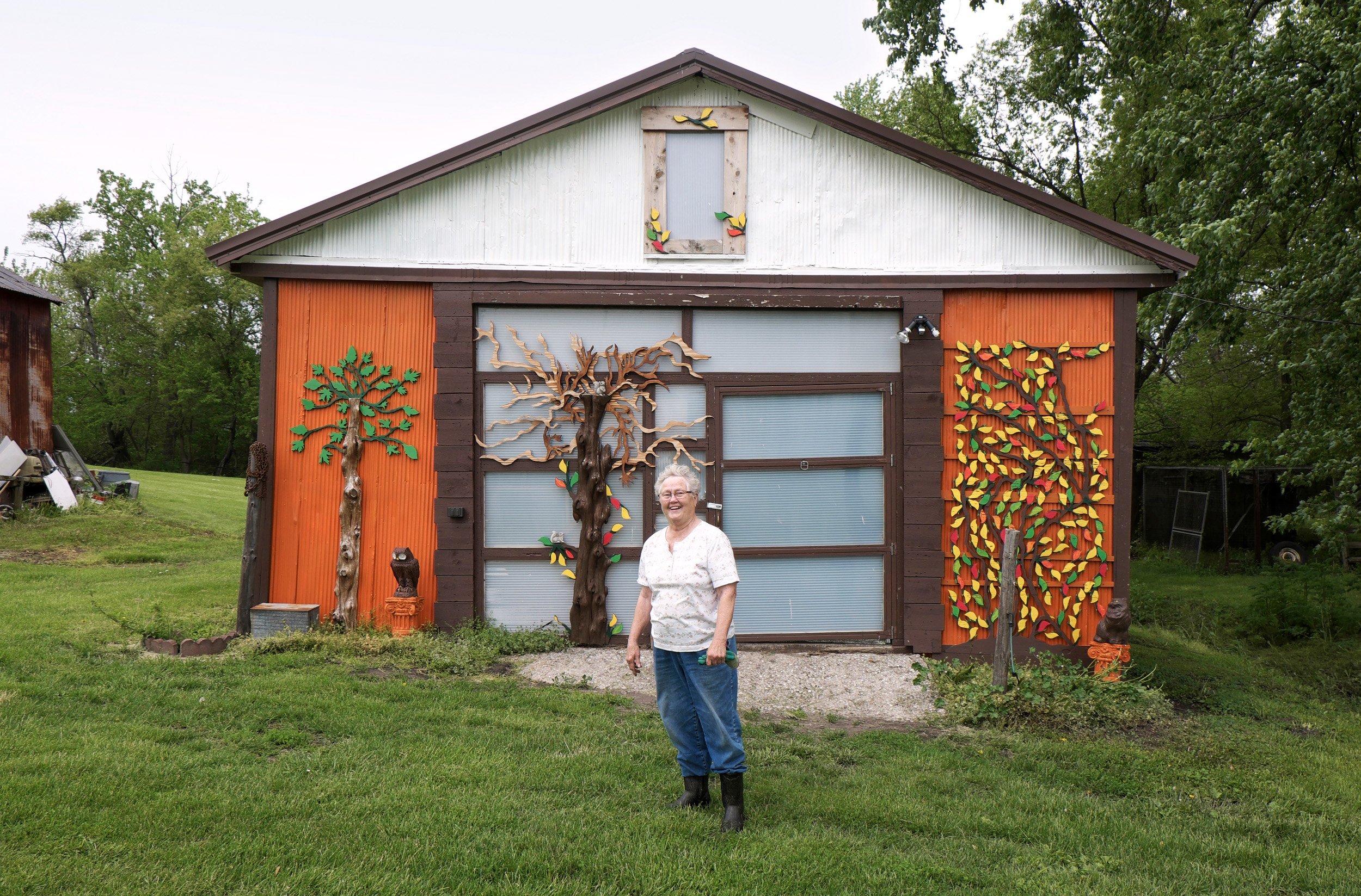  Woman standing by a garage decorated with artwork created by her son. Swan Lake, IL. May, 2016 