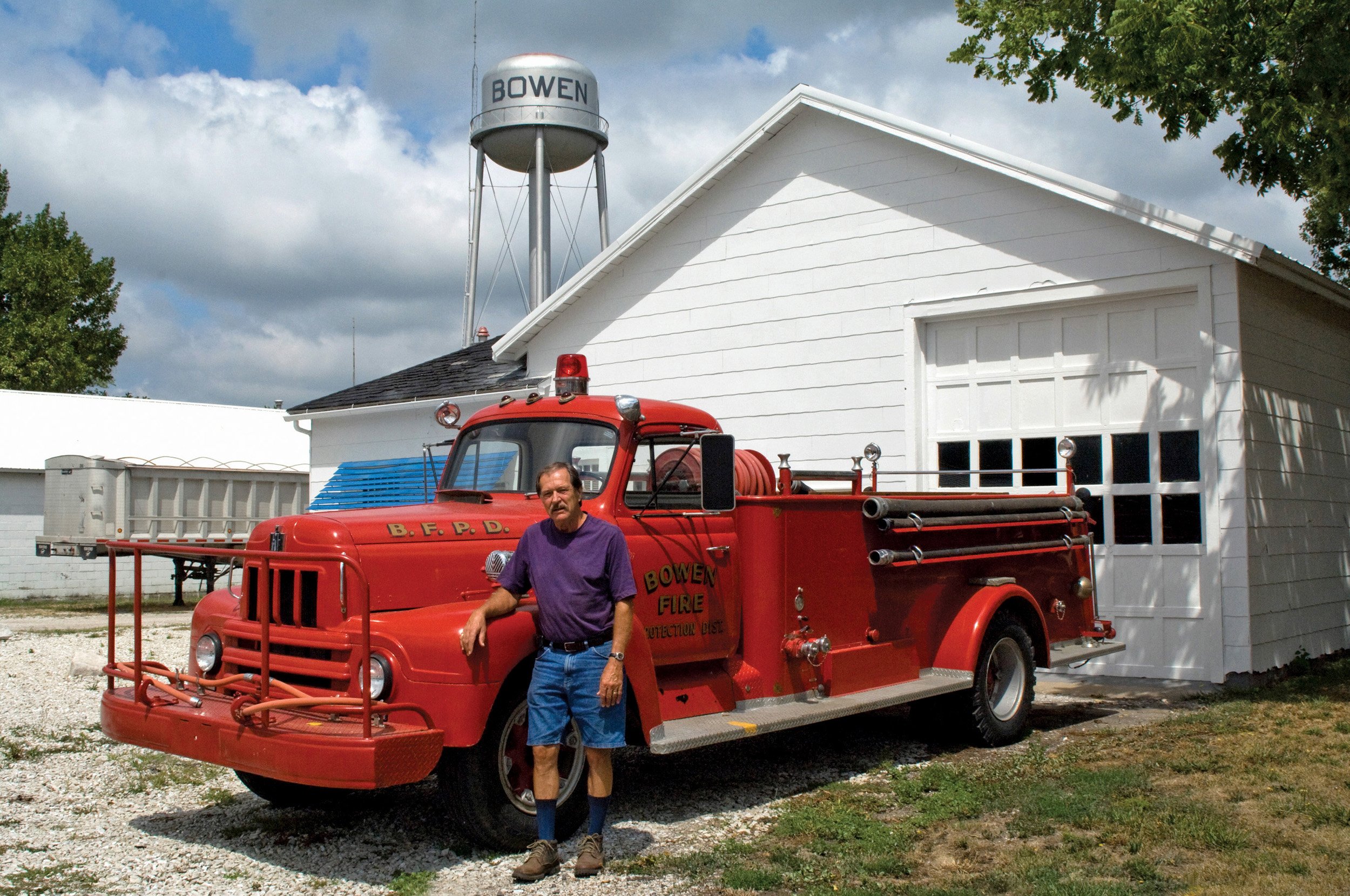  Mike Koch, standing by an antique Bowen fire truck and th white building where the Koch trucking and feed business was located. Bruce grew up with Mike. Bowen, IL. August 2012.  