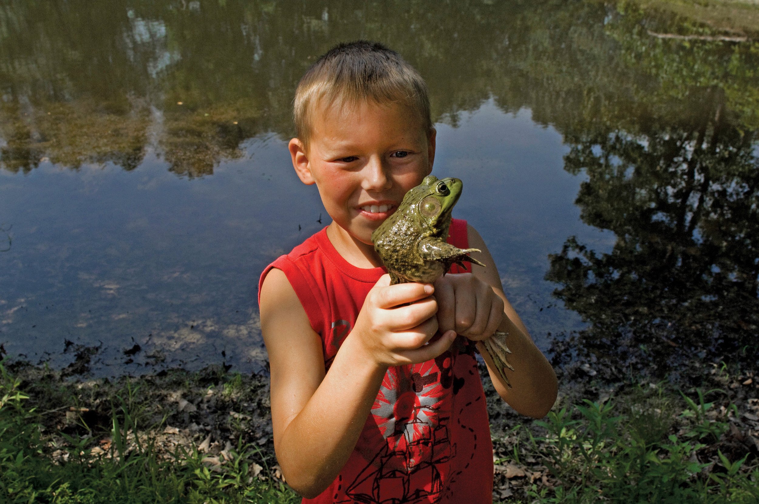  Boy holding a frog in front of a pond at a church camp. Timewell, IL. June, 2012 