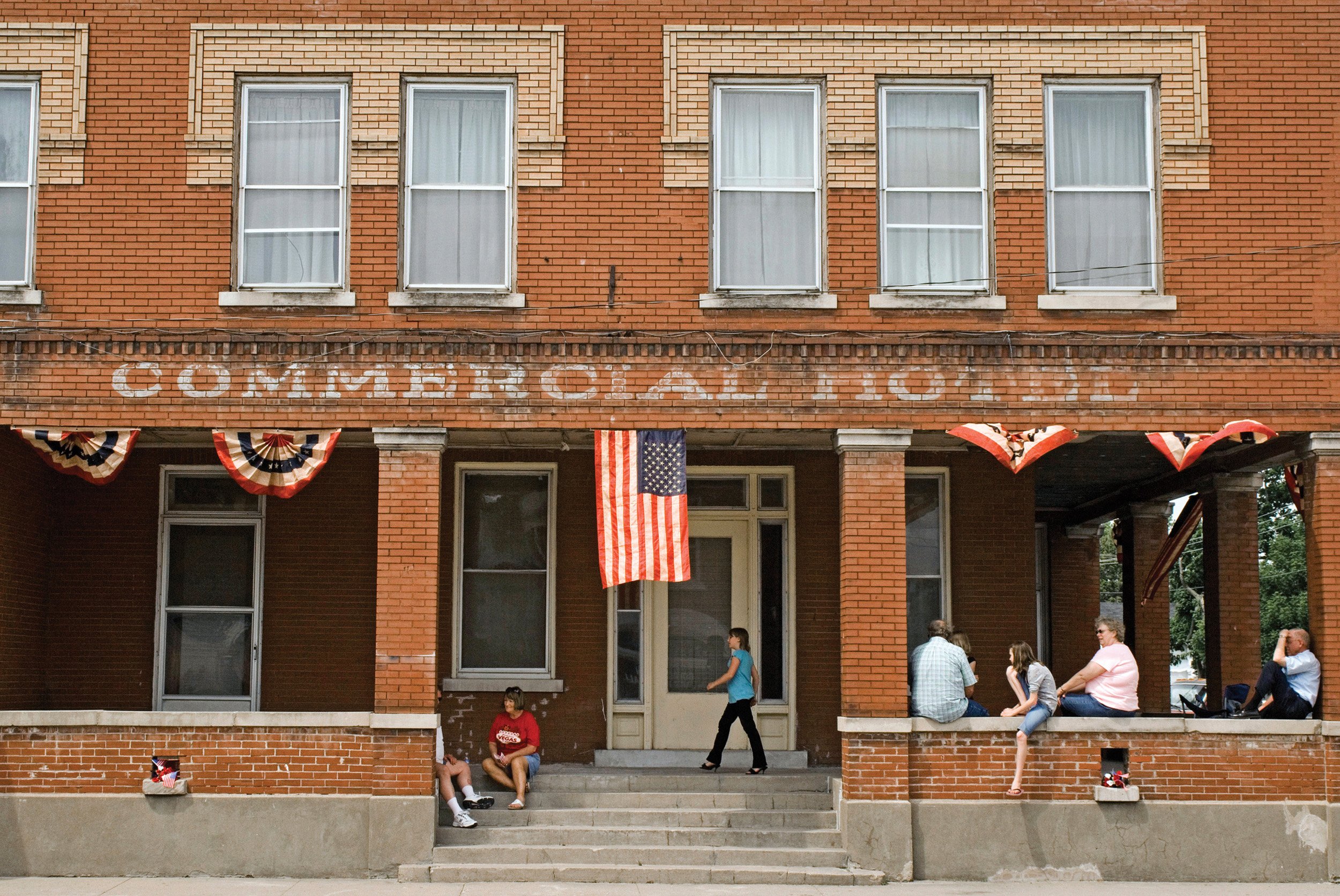  People sitting on the porch of the now defunct Commercial Hotel. People of Bowen had gathered to celebrate the completion of the Bowen Veterans Memorial. Bowen, IL. May, 2009 