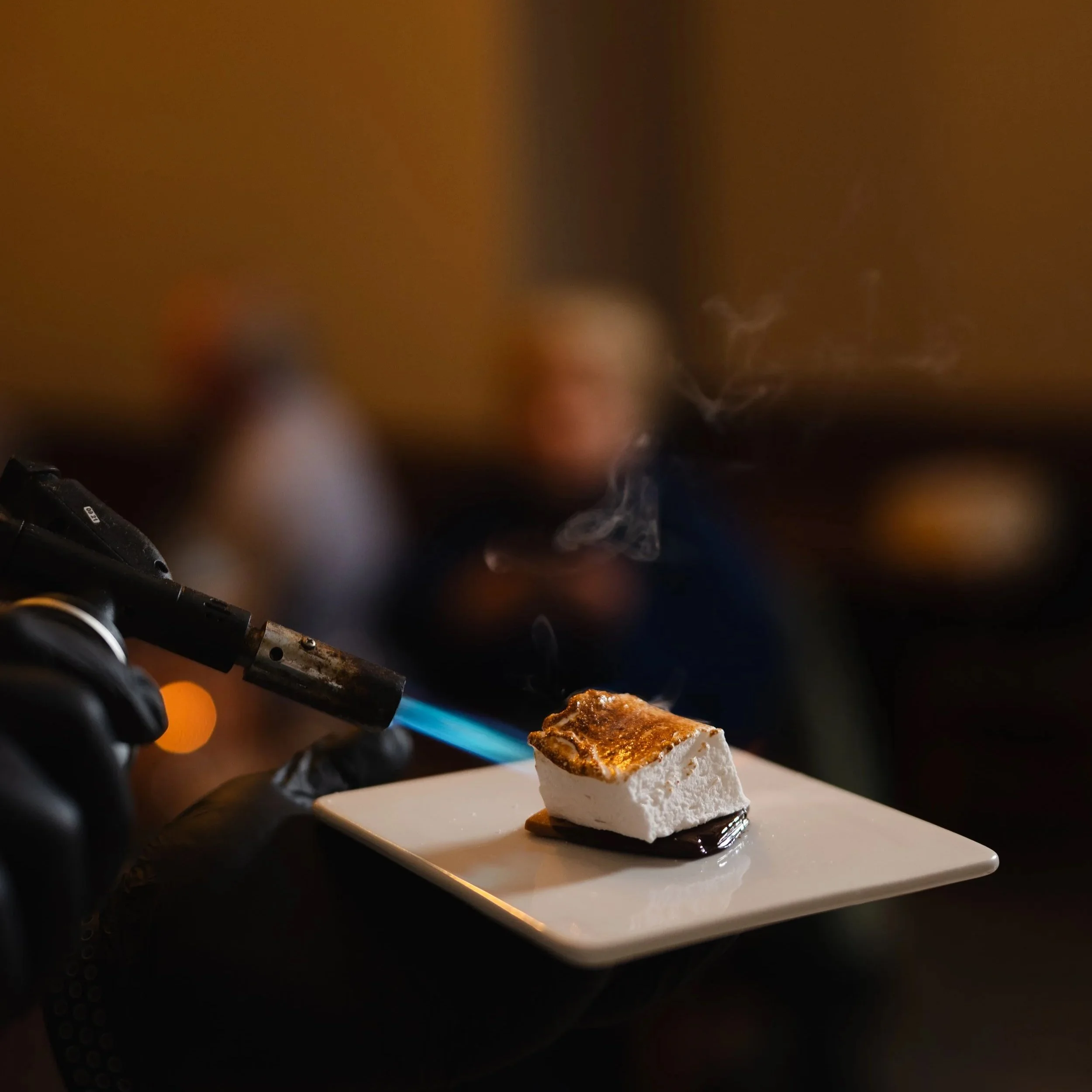 A fork with a piece of caramelized sugar or similar substance near a flame, on a white surface.