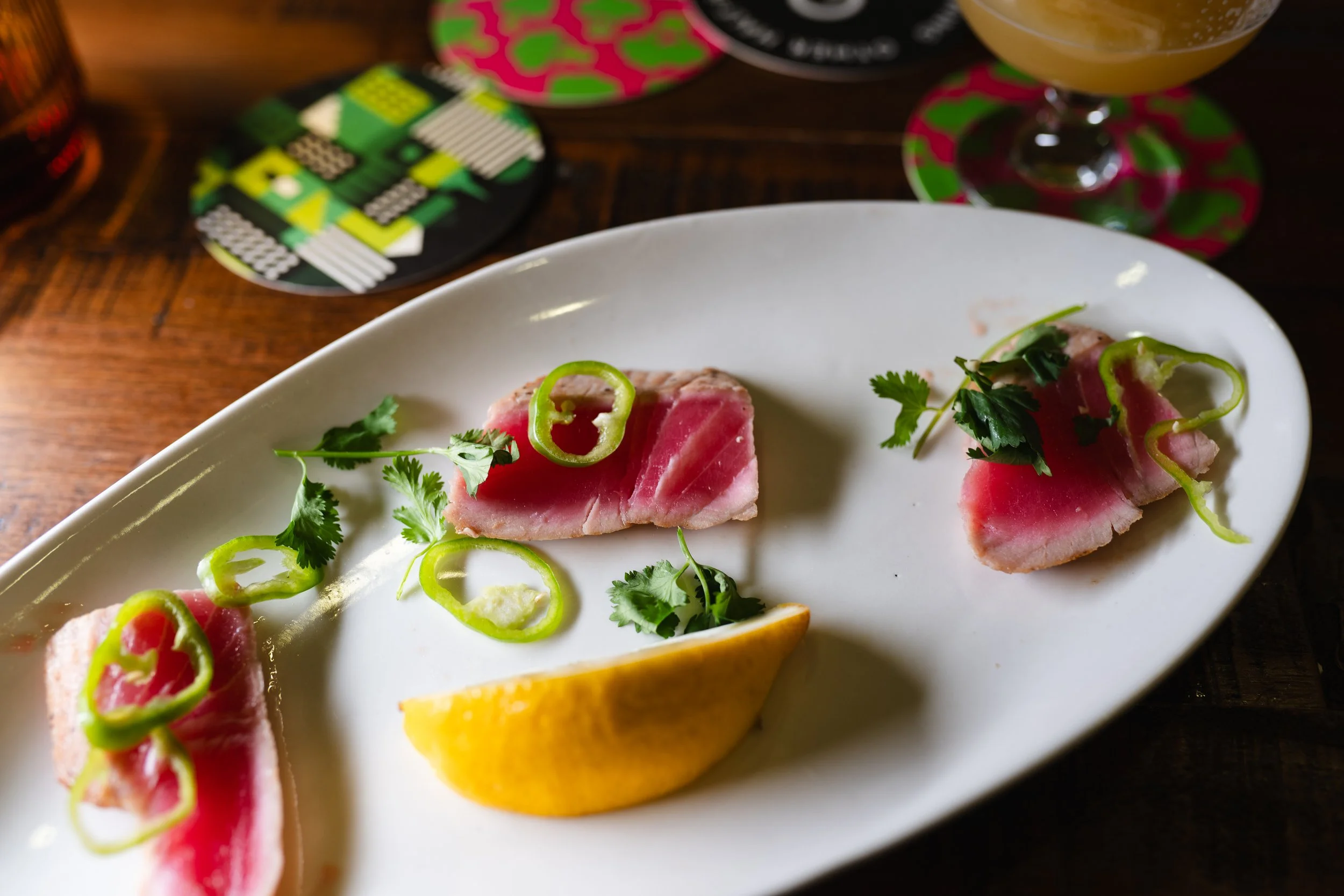 Sashimi on a white plate with green and yellow garnishes, lemon wedge, and sliced green peppers.