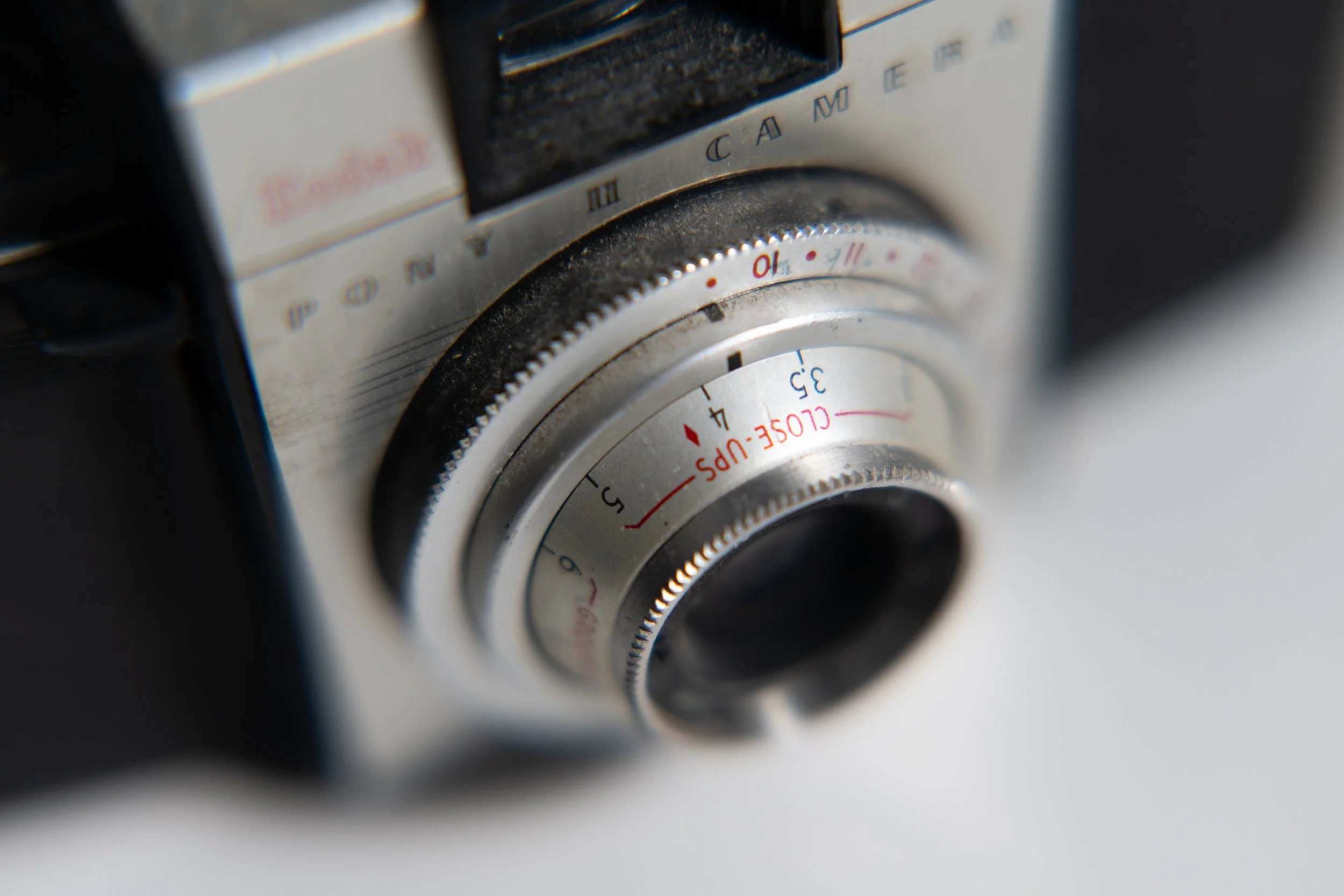 Close-up of a vintage film camera lens with manual focus and aperture adjustment rings, showing detailed markings and a slightly worn appearance.