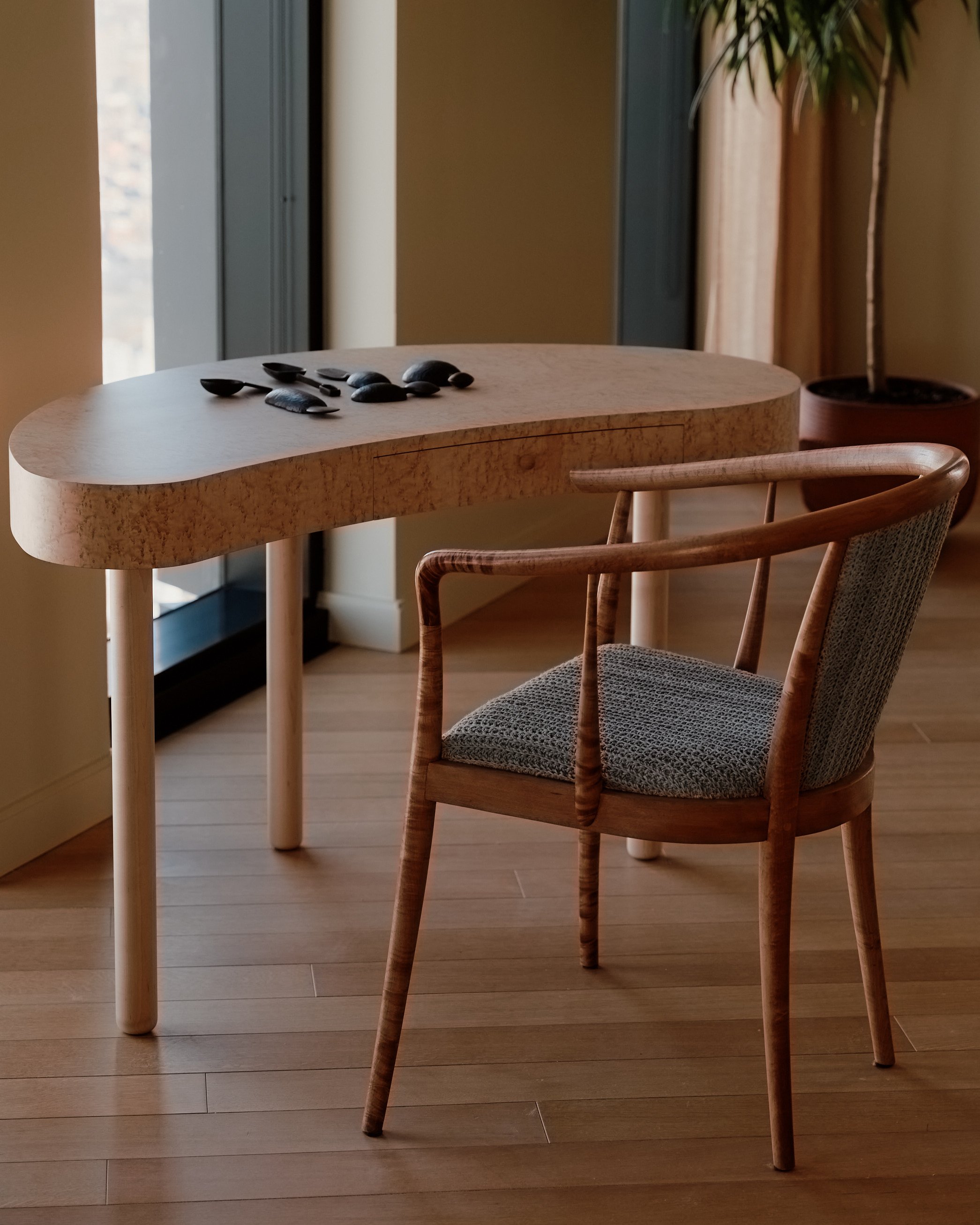 Triad Desk in Birdseye Maple, sitting against windows with an arrangement of hand carved spoons on top.