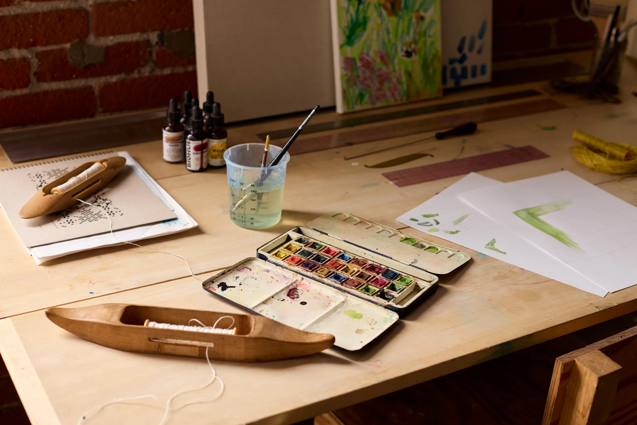 Radnor Represented  Artist, Rachel DuVall's desk filled with paint, threads and a weaving shuttle.