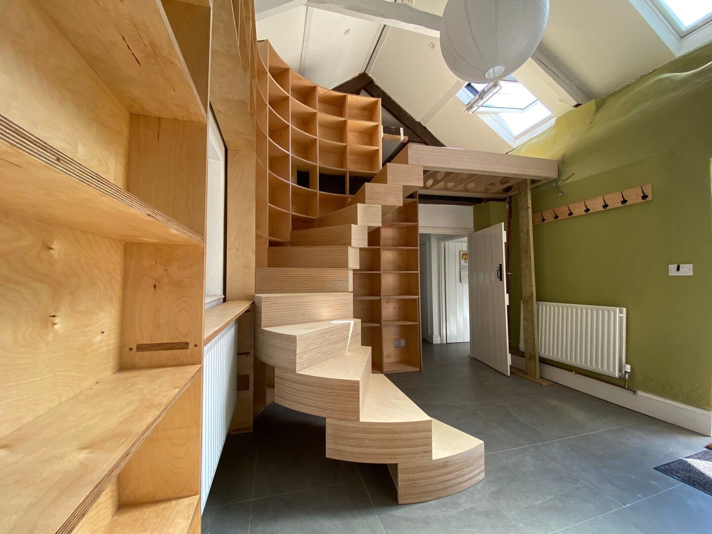 A birch plywood spiral staircase supported and cantilevered from a curved corner bookshelf. 
@ammonite.designs painstakingly measured the space and designed the stairs to tie into the existing walls while remaining a free-standing structure inside a 