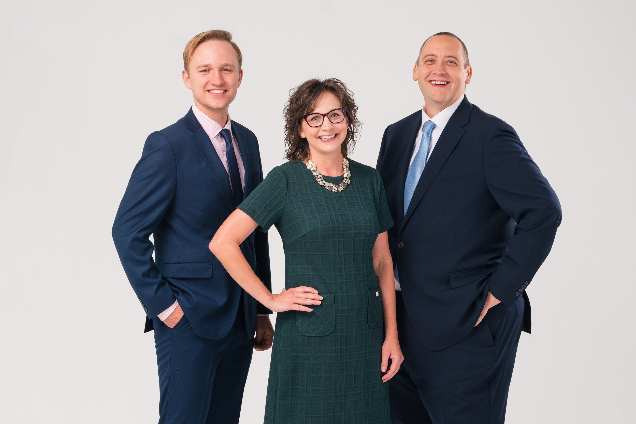 two men wearing blue suits and one woman wearing a green dress