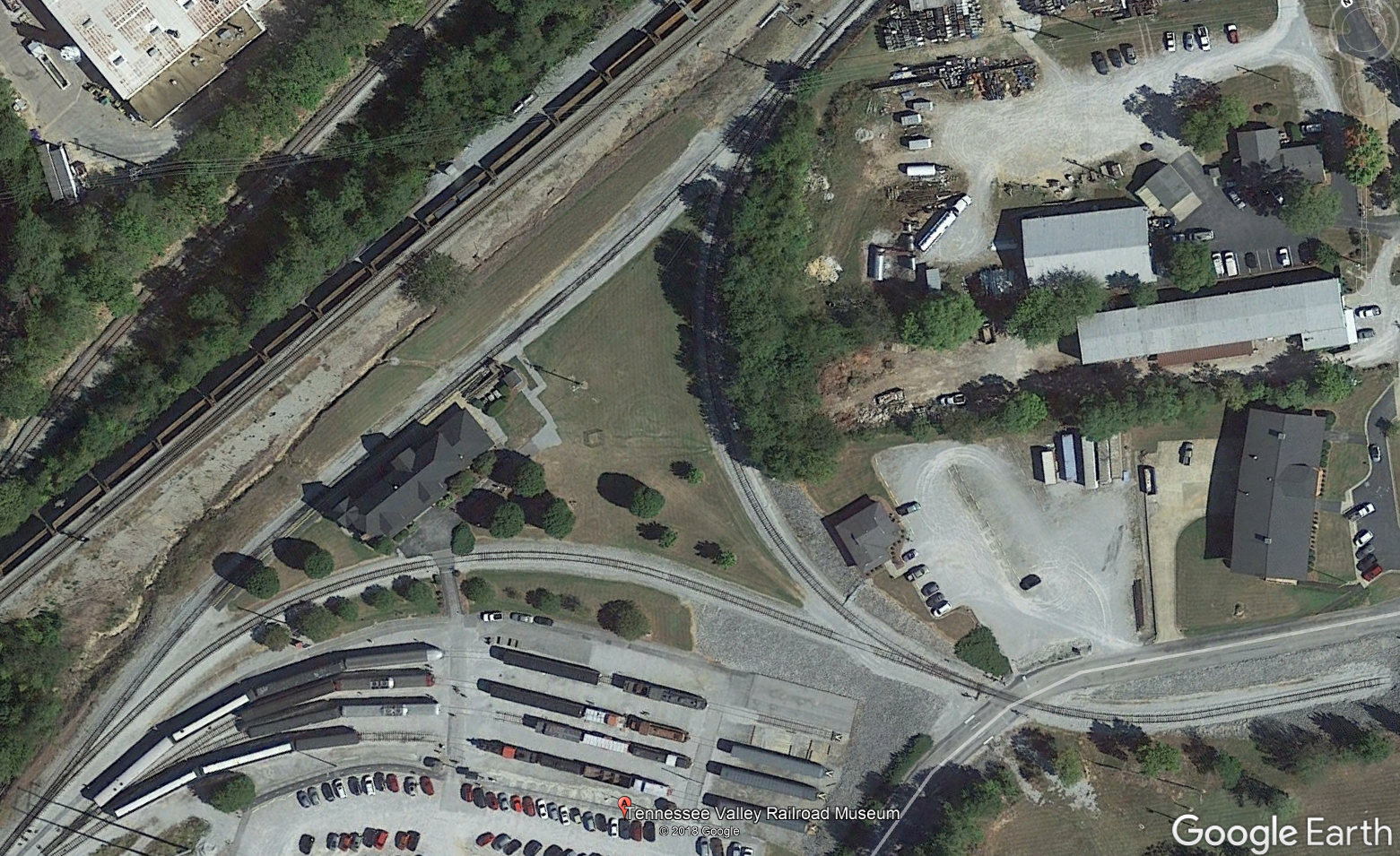 This satellite photo shows the wye at Grand Junction Station. A train enters from the lower left, and pulls up to the station along the top-left leg of the wye. After the passengers are loaded, the train pulls forward of the switch at the top center of the photo, then reverses along the curved track obscured by trees. The tail track in the lower right is just barely long enough to fit a locomotive and three passenger cars. Once the train is clear of the switch adjacent to the road crossing, it pulls forward along the lower leg of the wye, past the sidings of equipment on display, and returns to the track it came from in the lower left, now traveling in the opposite direction.