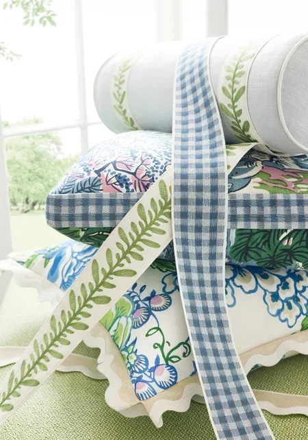 Stack of decorative pillows with patterned ribbons on a bed near a window.