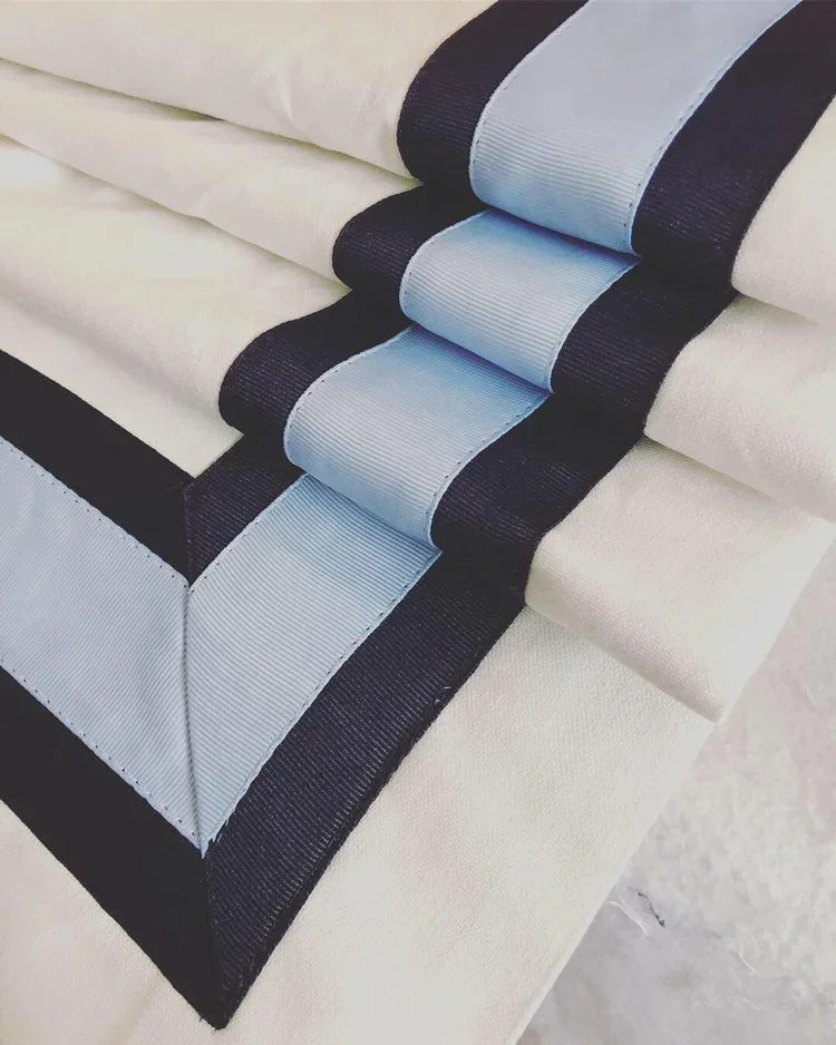 Stacked cream-colored fabric with black and light blue accents, showing a close-up of folded textiles with black trim.