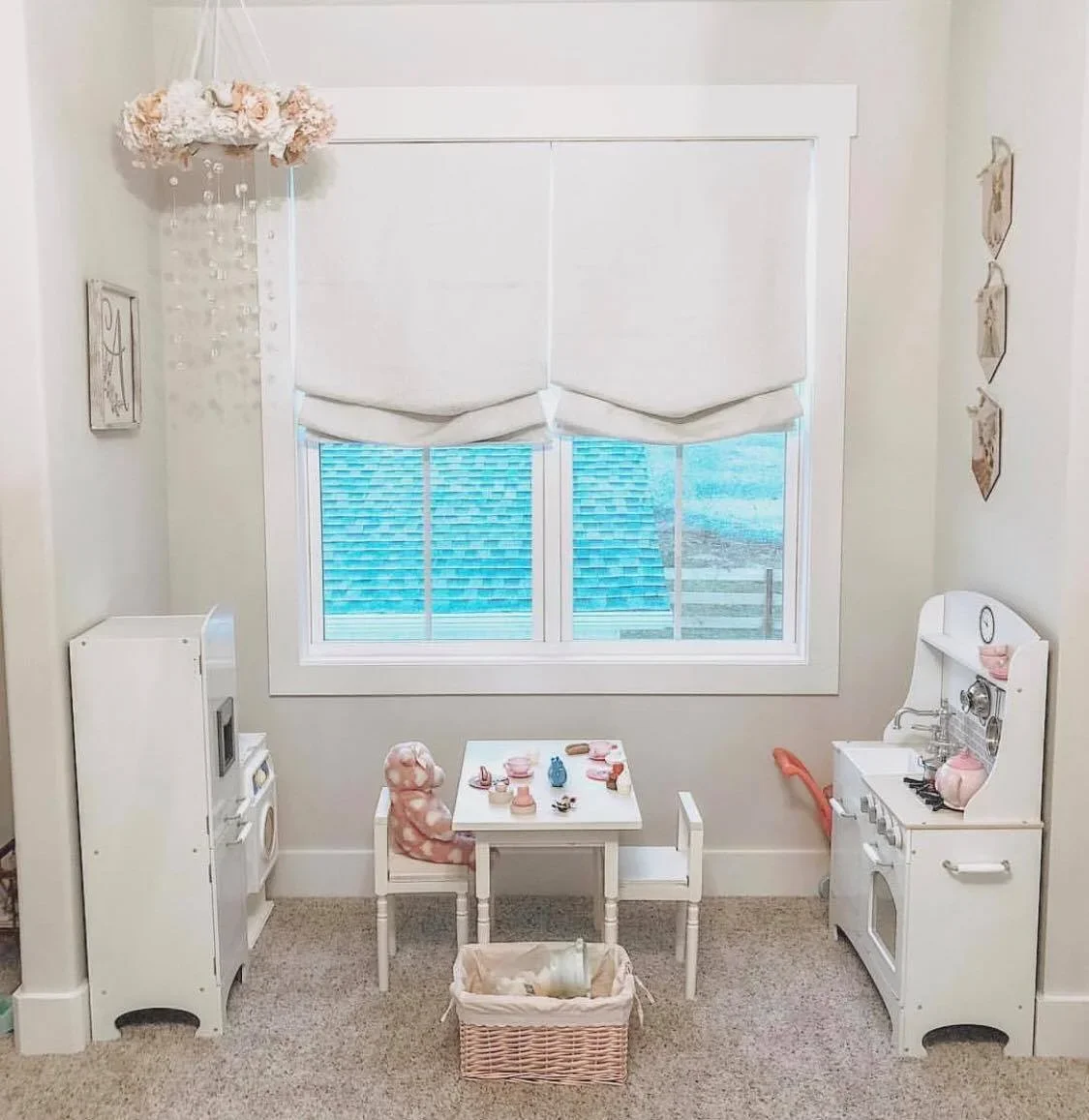 Little girl and boy doll size play kitchen set with a small table, chairs, and a basket in a cozy corner, resembling a child's play area.