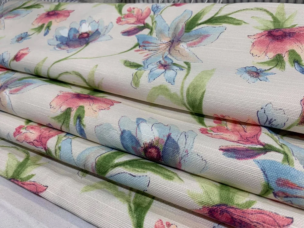 Folded fabric with a floral watercolor pattern featuring pink, blue, purple, and green flowers on a white background.