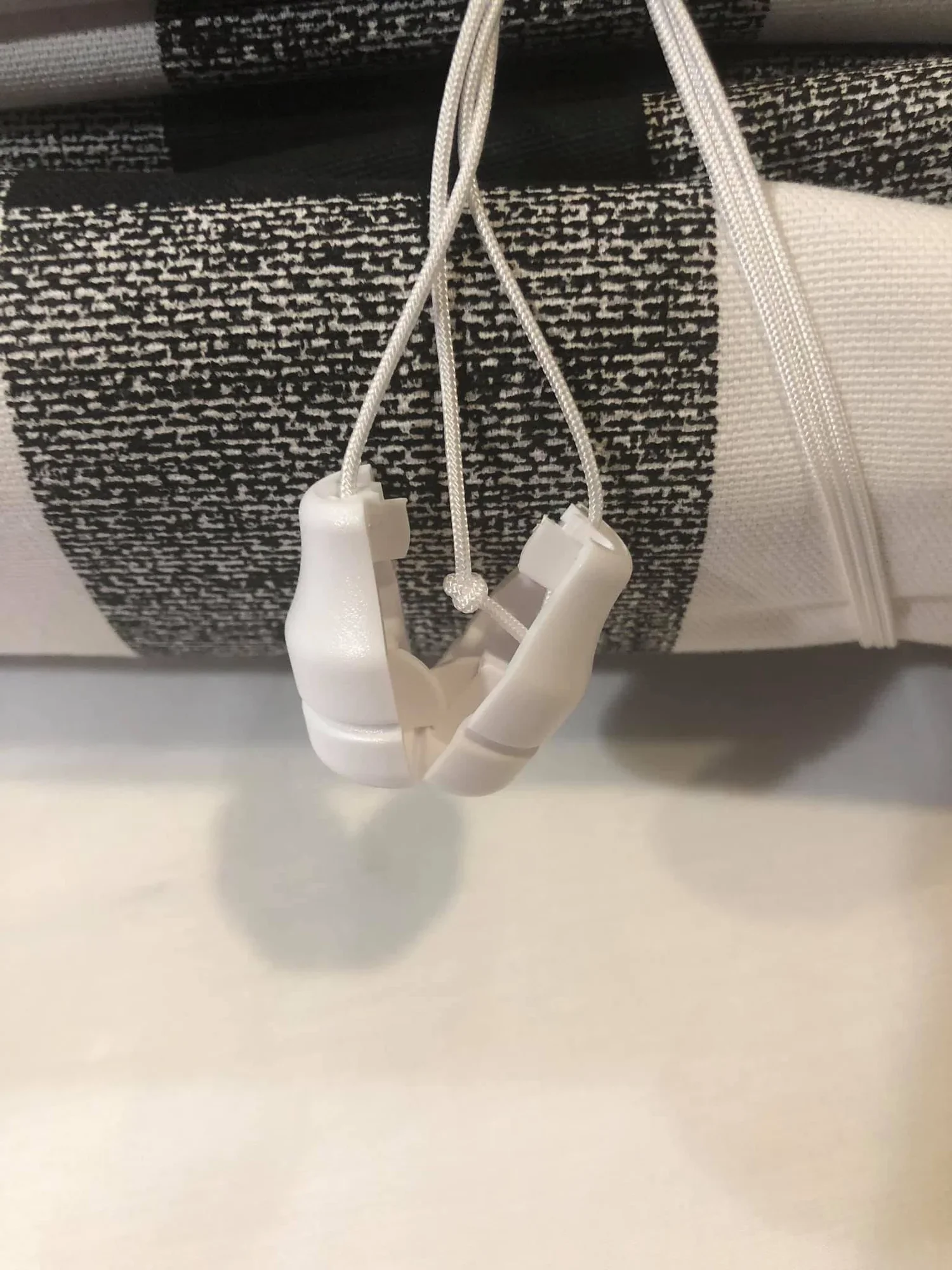A close-up of a black and white patterned fabric with a white electrical cord and white plastic MRI head coil attachments hanging in front of it.