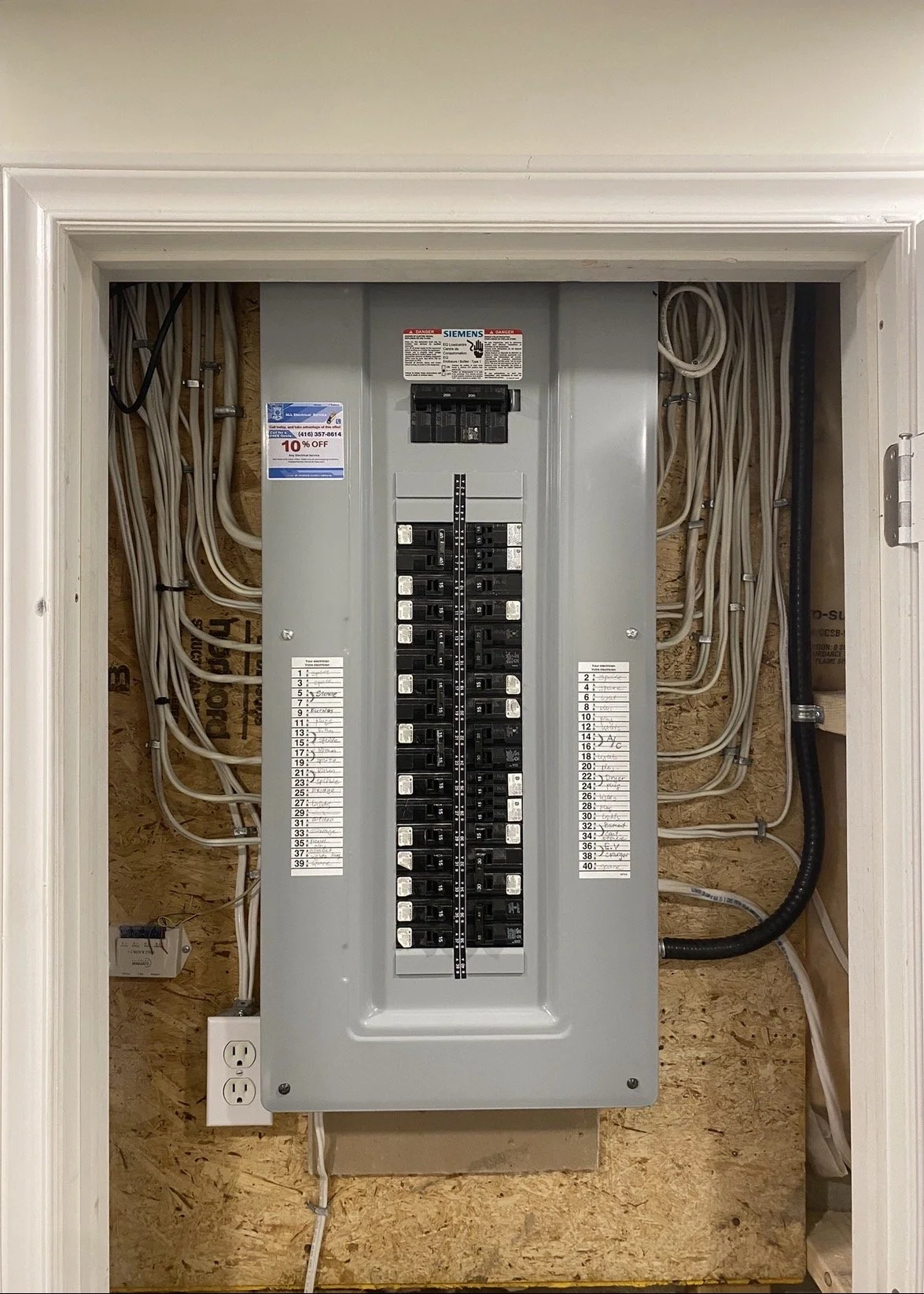 Main electrical panel with circuit breakers inside a closet, with visible wiring and a power outlet at the bottom.