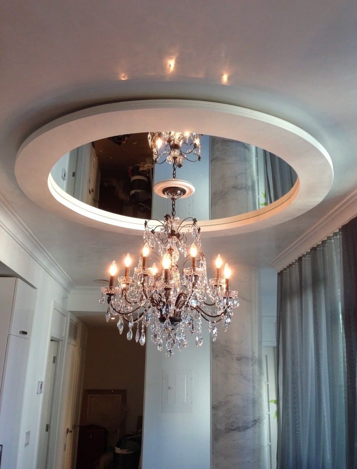 Completed installation project of a crystal chandelier mounted on a custom mirrored circular recessed ceiling.