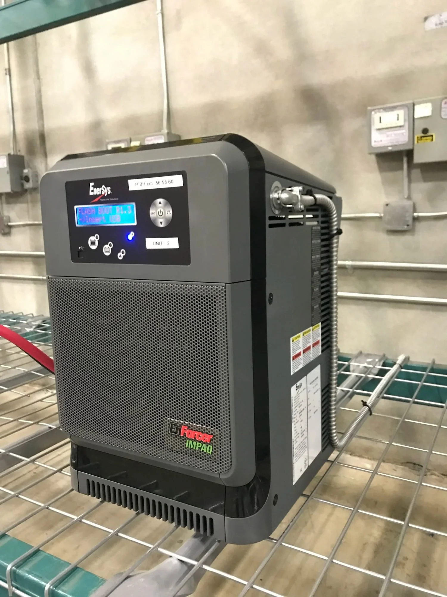 Installation of an EnerSys EnForcer IMPAQ industrial battery charger system on a warehouse metal rack.