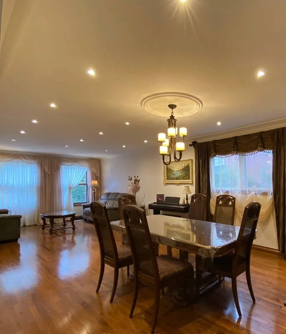 Modern recessed LED lights and chandelier lighting professionally installed in a residential living and dining room.