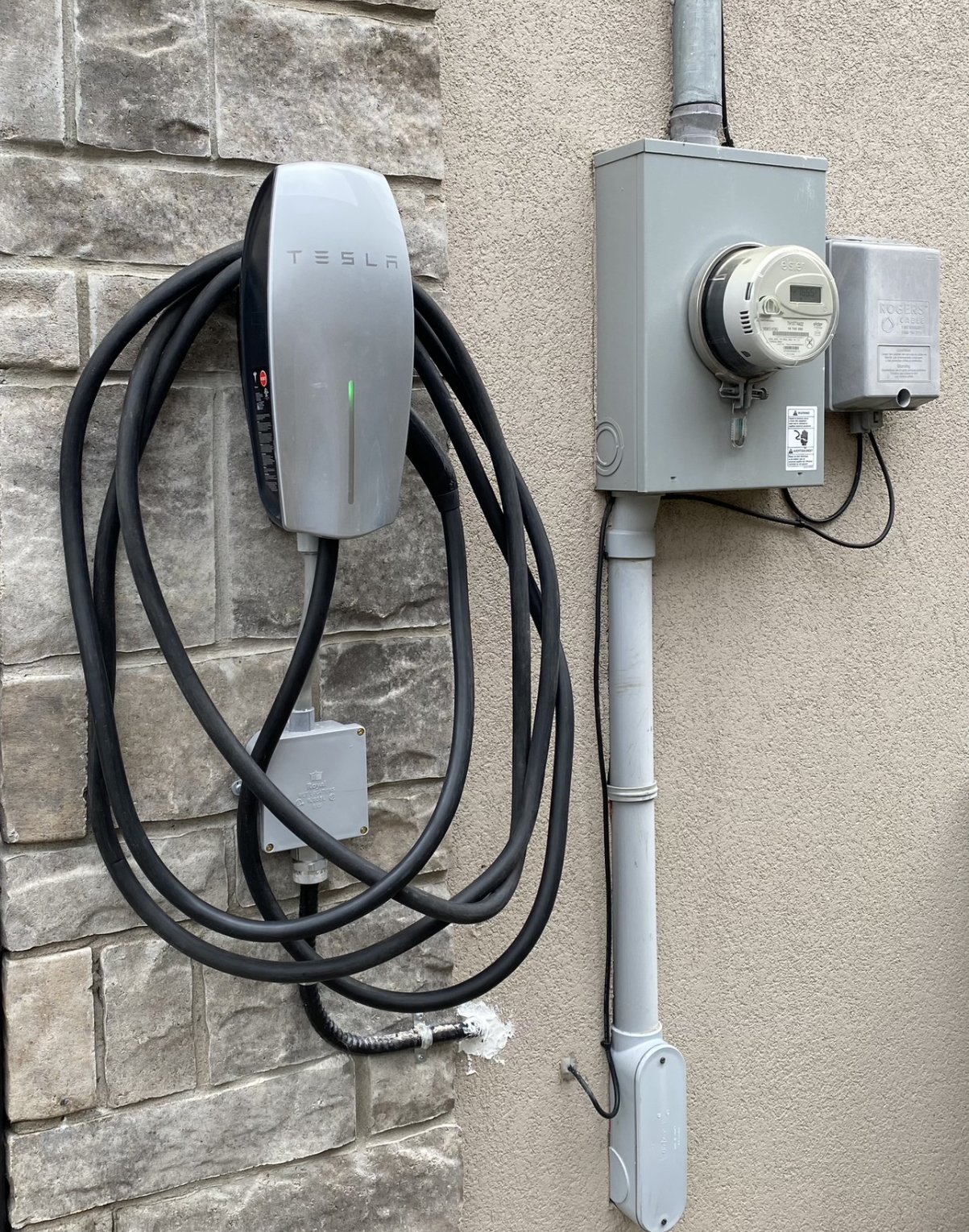 A Tesla electric car charging station installed on the outside wall of a house allows you to charge your electric car in any weather and season.