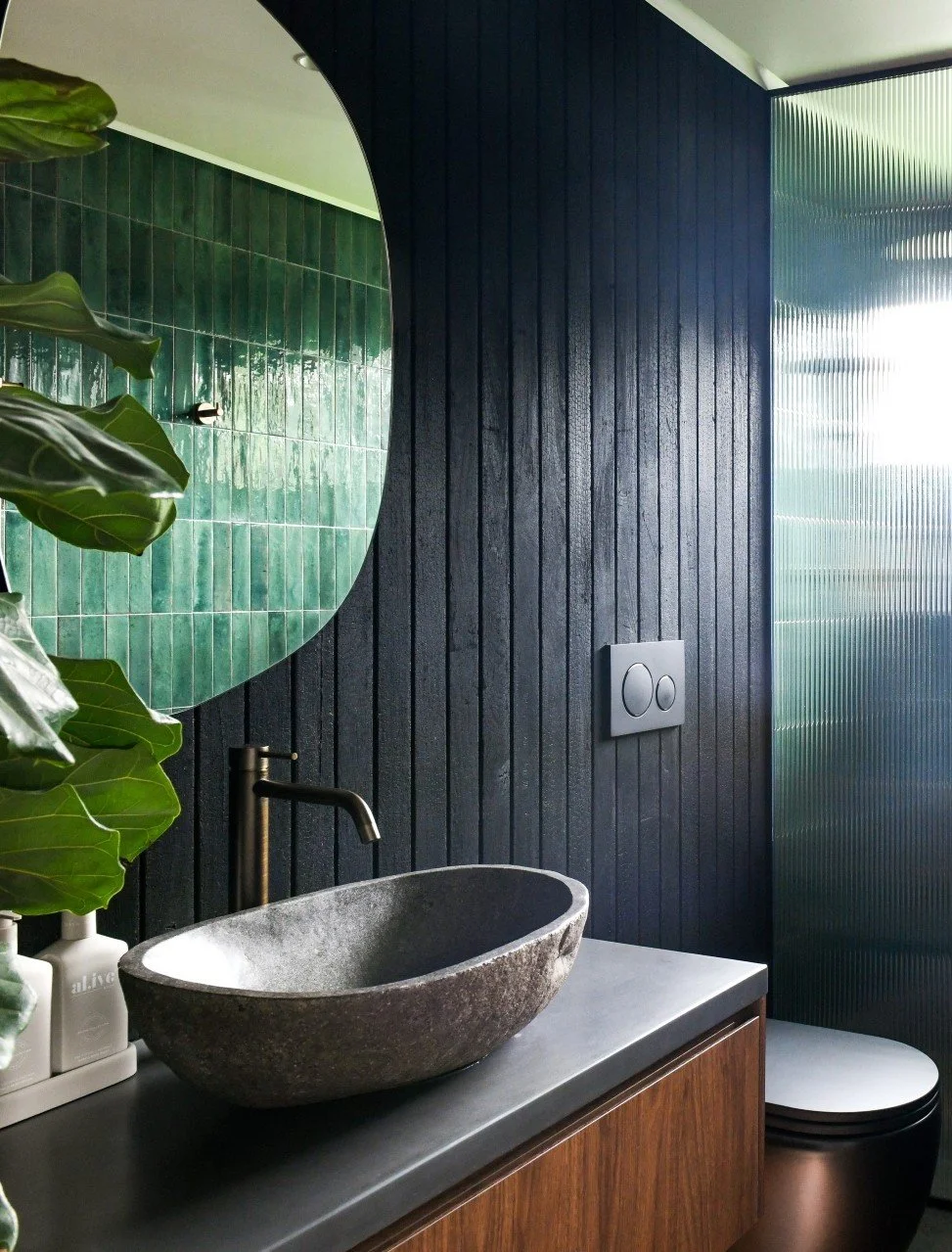 Dark moody bathroom with black timber and dark green tiles and timber vanity with natural stone basin.