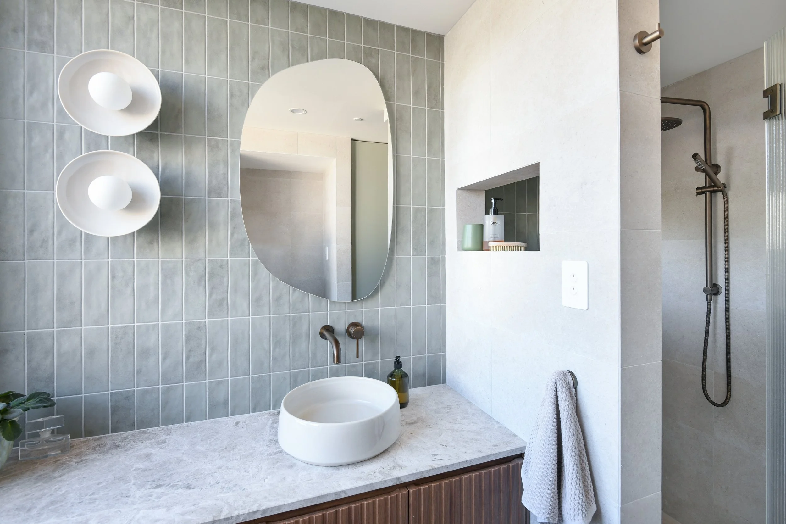 Neutral light grey bathroom with soft blue subway feature tile, timber vanity and round wall scones. 