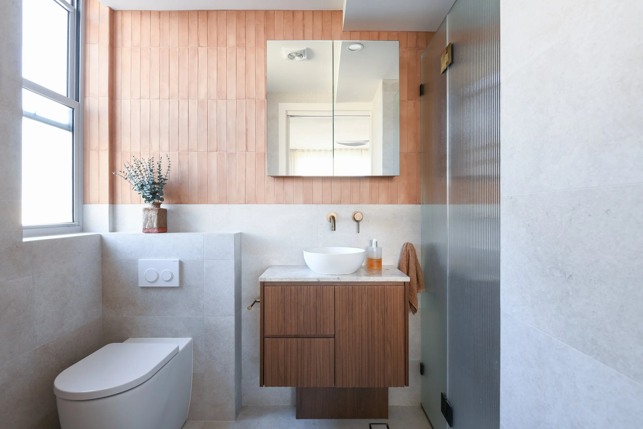Light grey tiled bathroom with pink feature tiles and a timber vanity.
