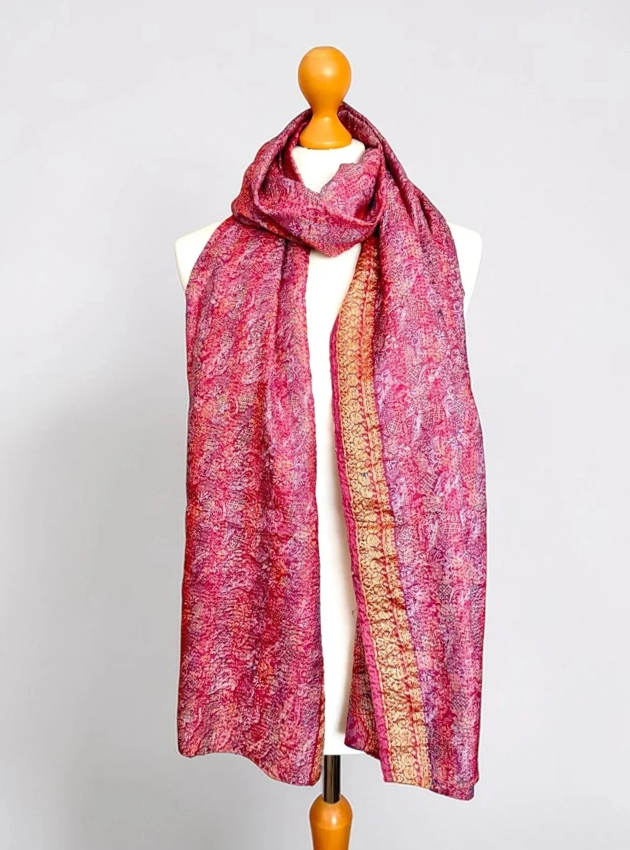 A long rectangular silk scarf with a gold thread border draped around a mannequin against a white backdrop