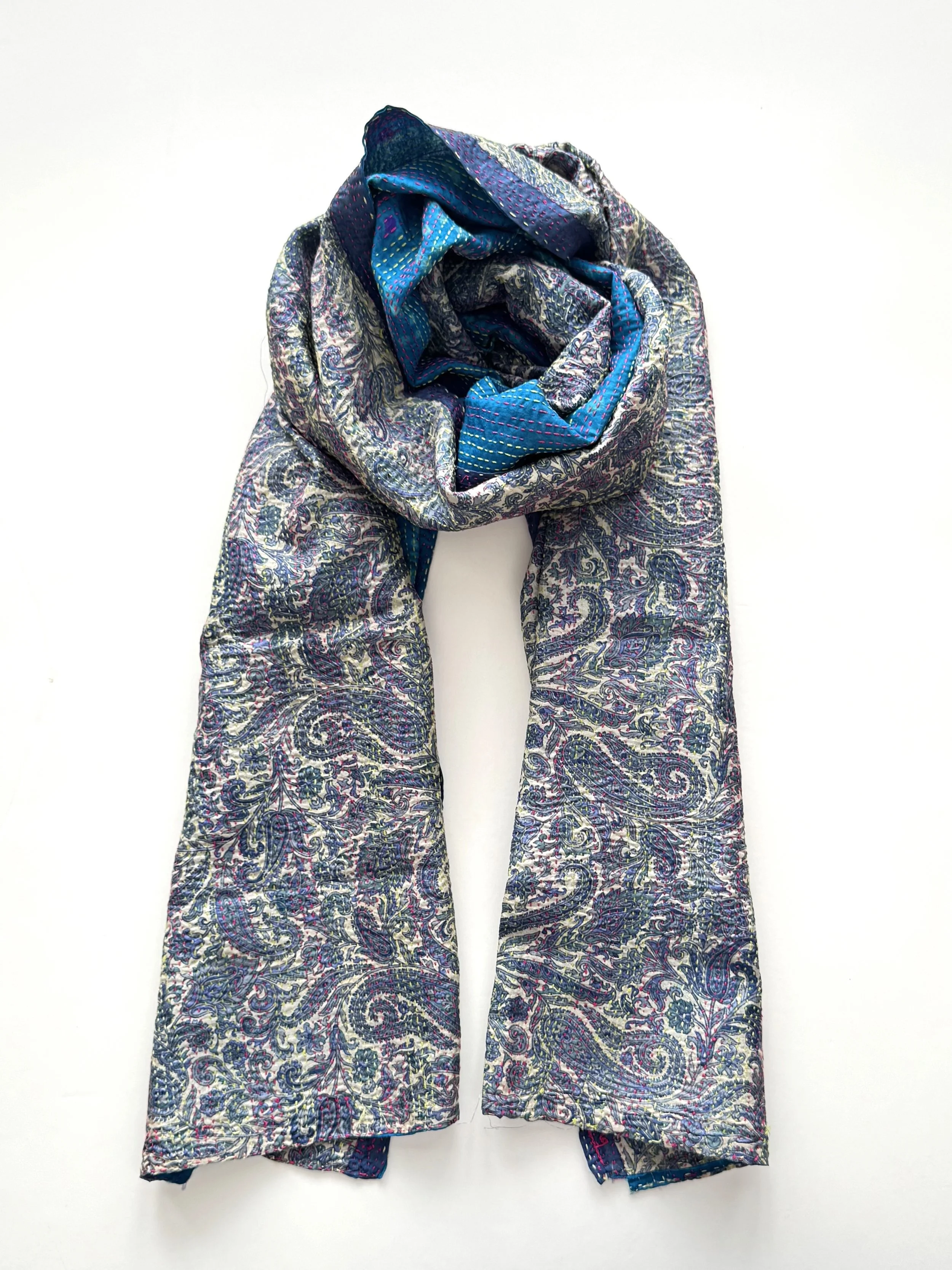 A folded scarf featuring a detailed blue and silver paisley pattern is displayed against a white background, creating an elegant and intricate look.