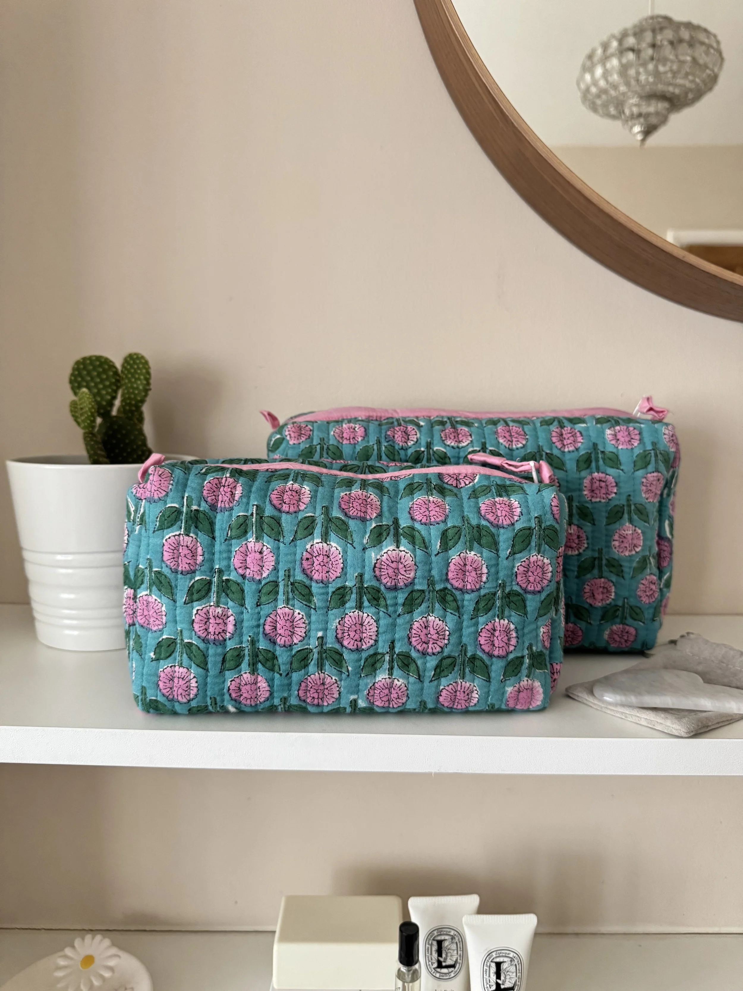 Two handmade cosmetic bags in blue with pink flowers resting on a white shelf under a mirror