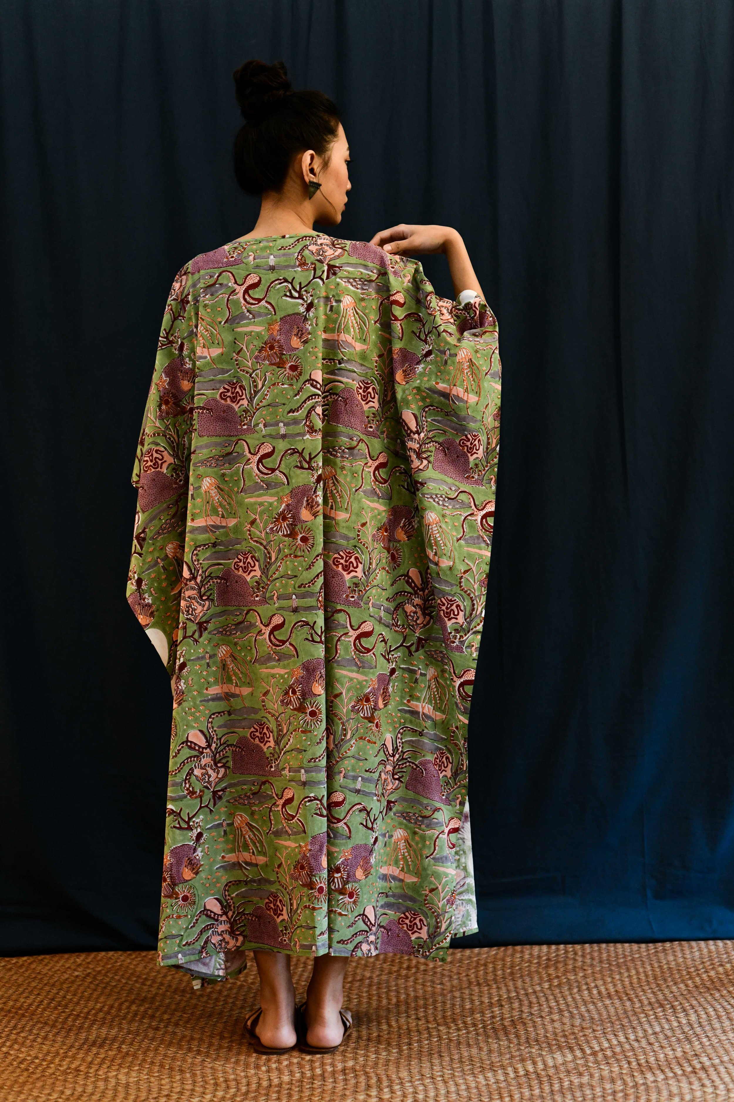 Back view of south asian female wearing a sea green cotton dress with nautical motifs of sea creatures in block print