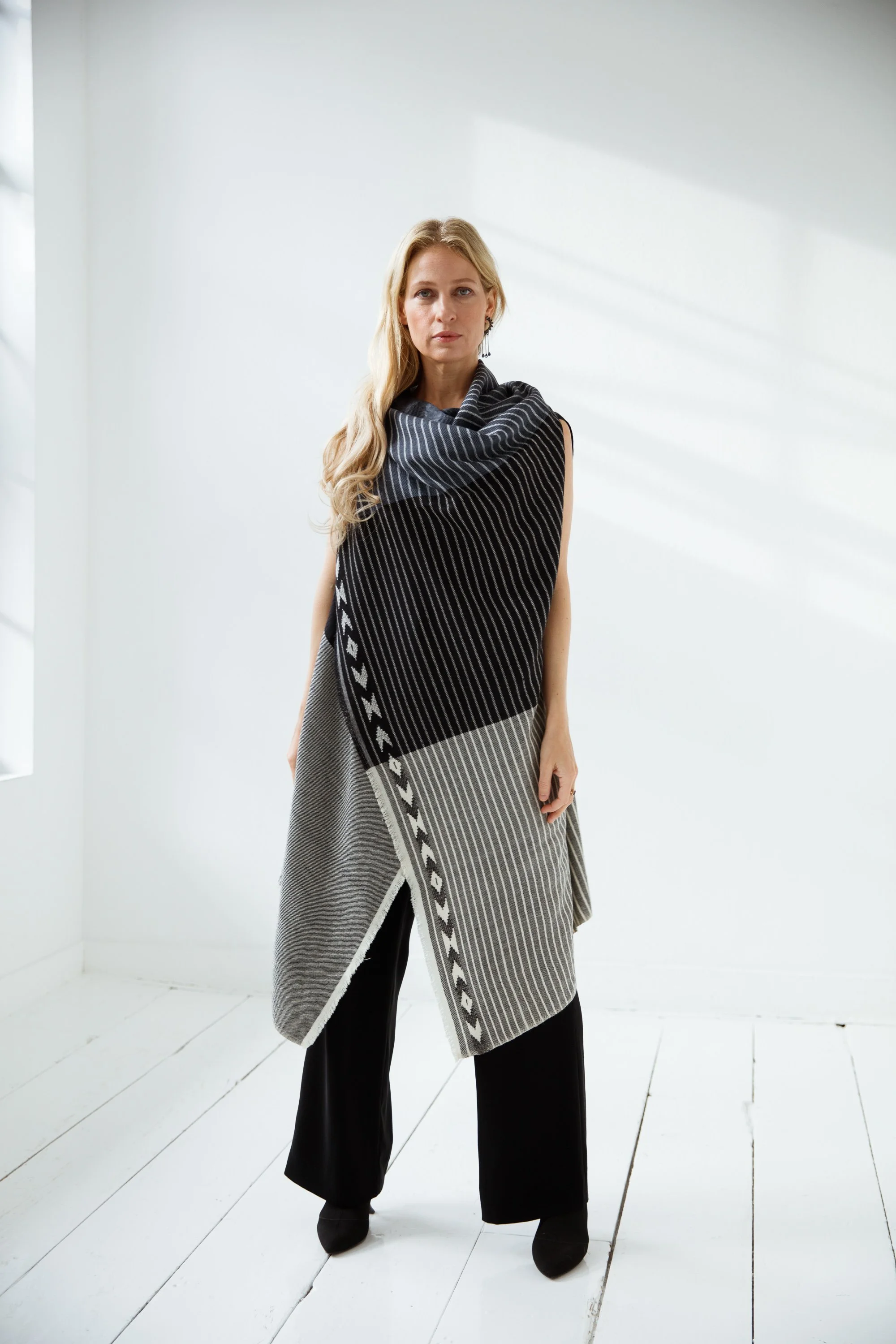 White female with blonde hair wearing a black and white soft, wool artisan woven cape poncho