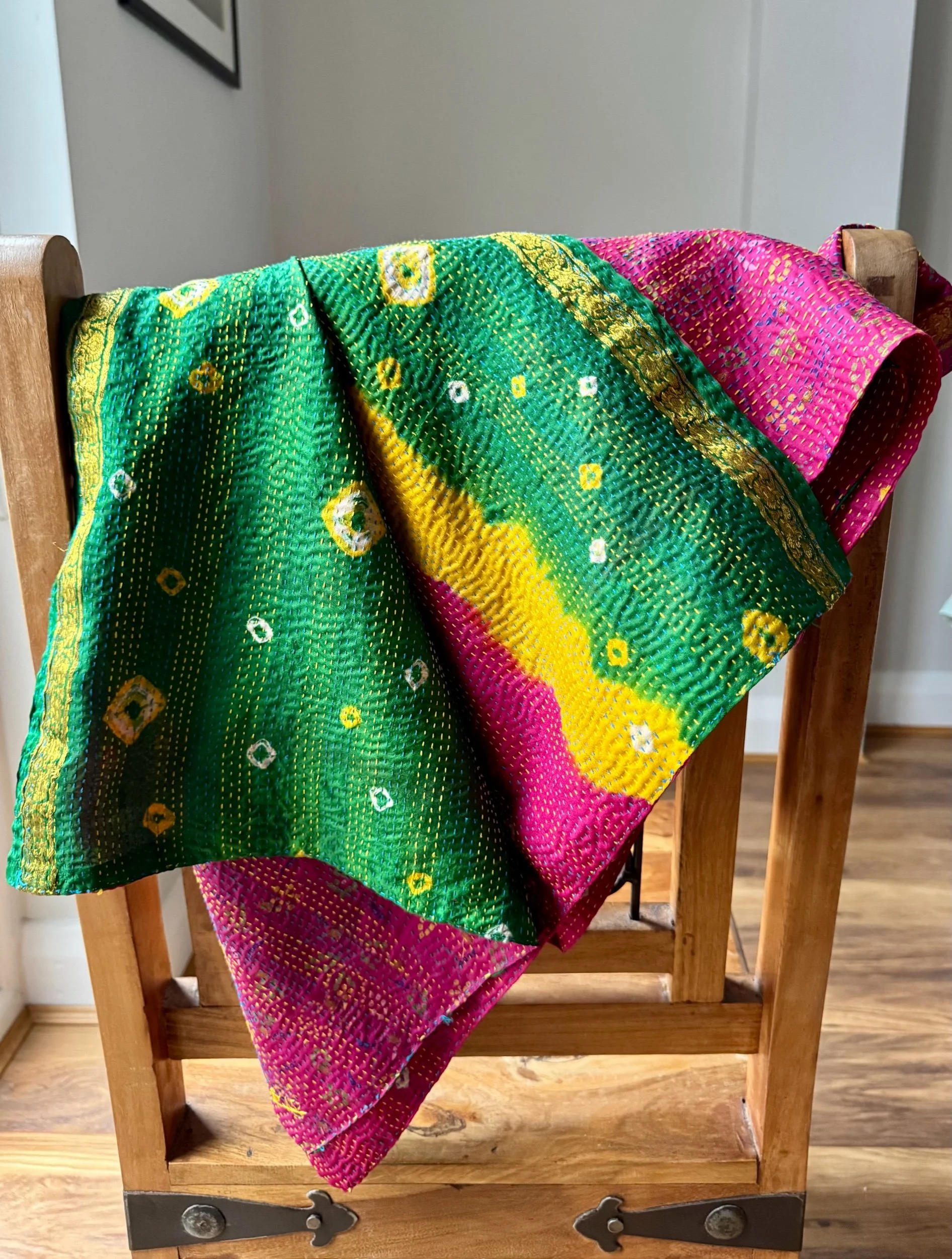 A colourful kantha sari scarf draped over a wooden Jali style chair, the scarf has the name of the artisan embroidered in red and features hand embroidered kantha stitch all over