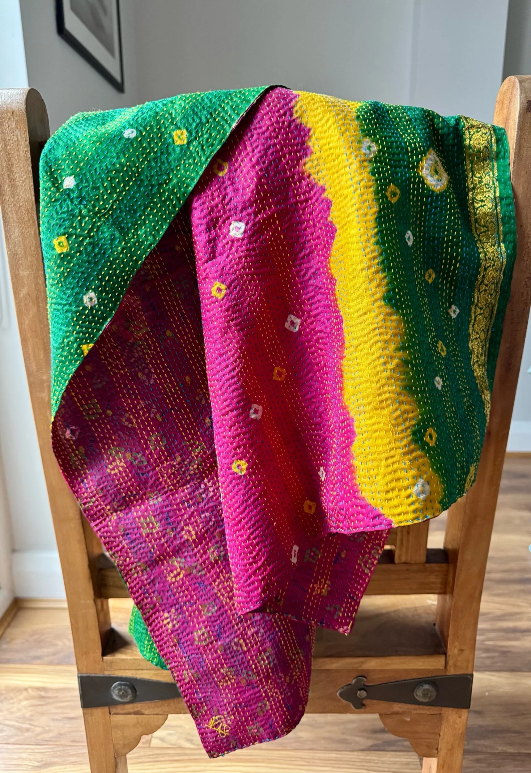 A colourful kantha sari scarf draped over a wooden Jali style chair, the scarf has the name of the artisan embroidered in red and features hand embroidered kantha stitch all over