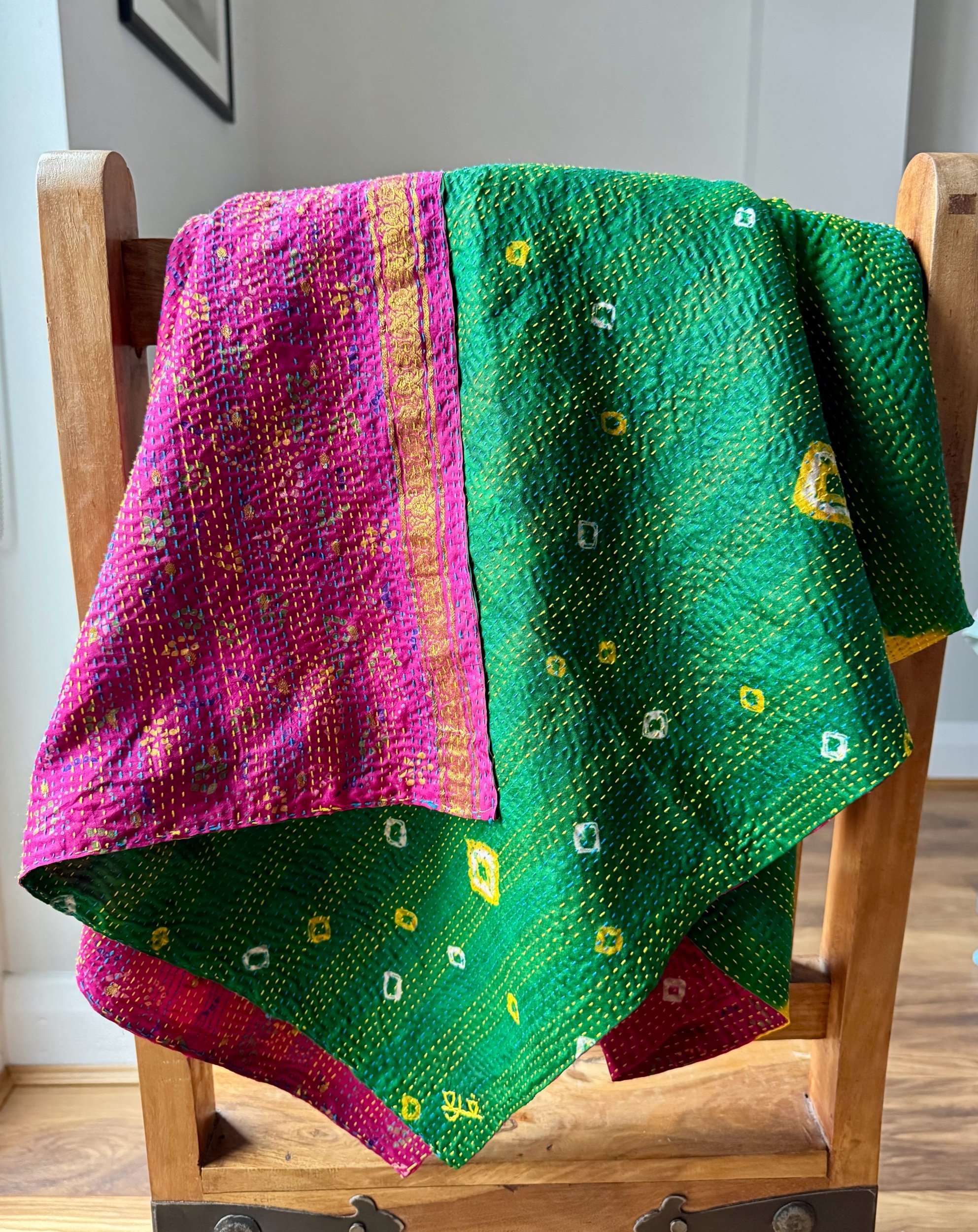 A colourful kantha sari scarf draped over a wooden Jali style chair, the scarf has the name of the artisan embroidered in red and features hand embroidered kantha stitch all over