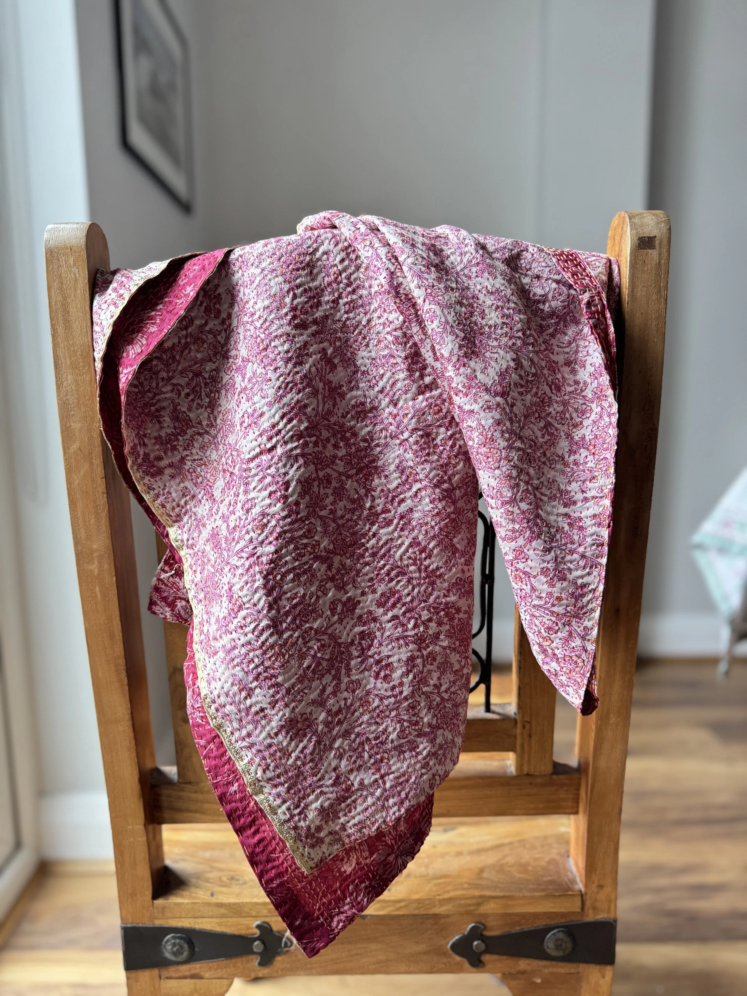 A colourful pink reversible kantha sari scarf draped over a wooden Jali style chair, the scarf has the name of the artisan embroidered in red and features hand embroidered kantha stitch all over.