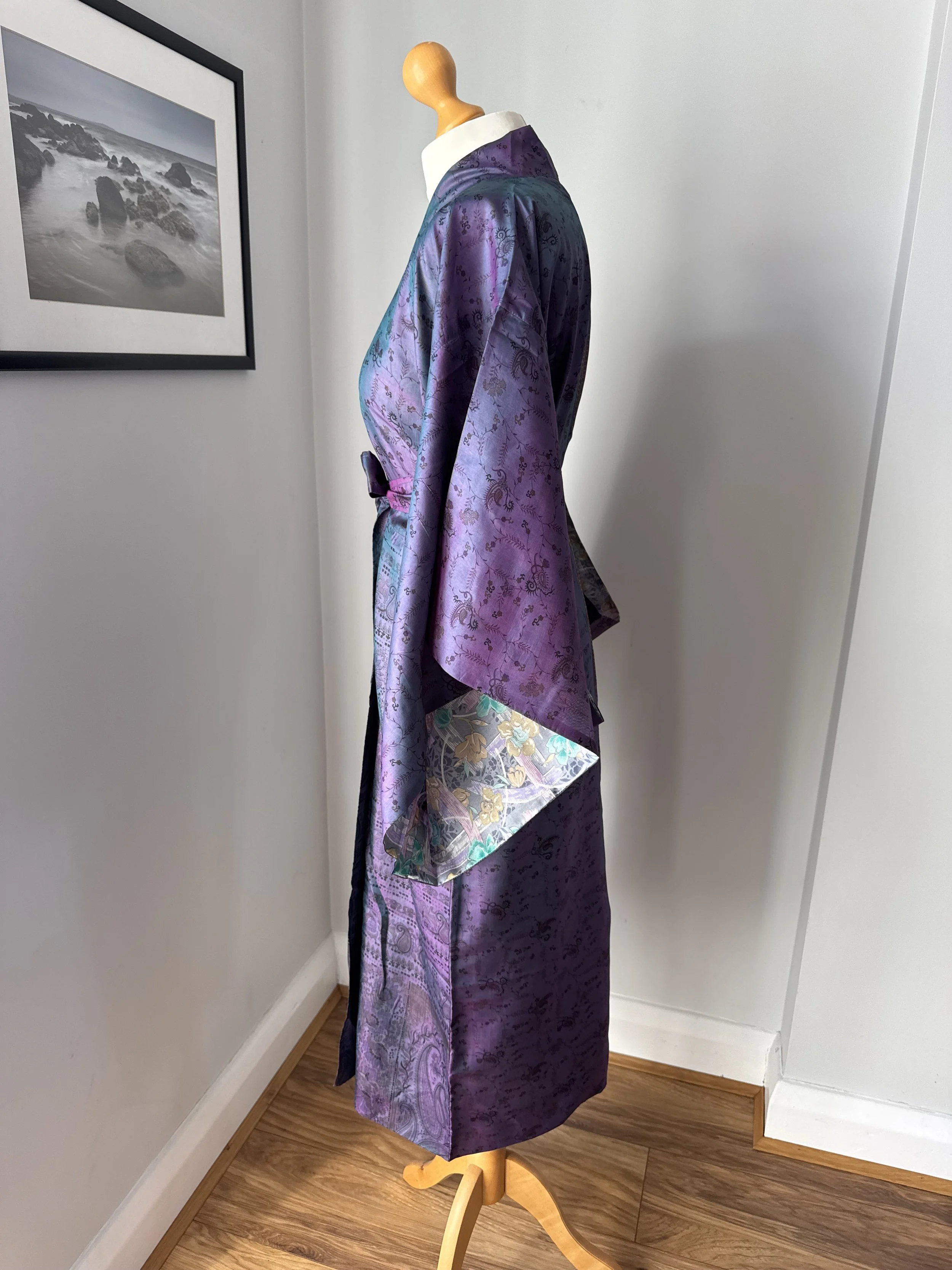 Side view of upcycled sari silk kimono robe in purple with contrasting light grey inside lining showing through the sleeves, draped over a mannequin against a grey wall