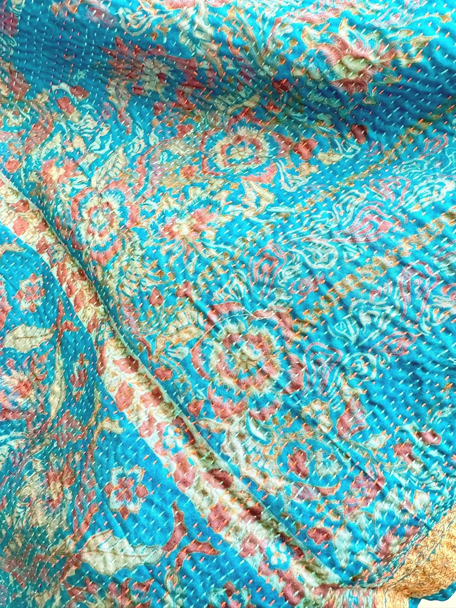 Close-up of a teal and coral floral patterned, quilted fabric with visible stitching throughout, showing folds and textures.