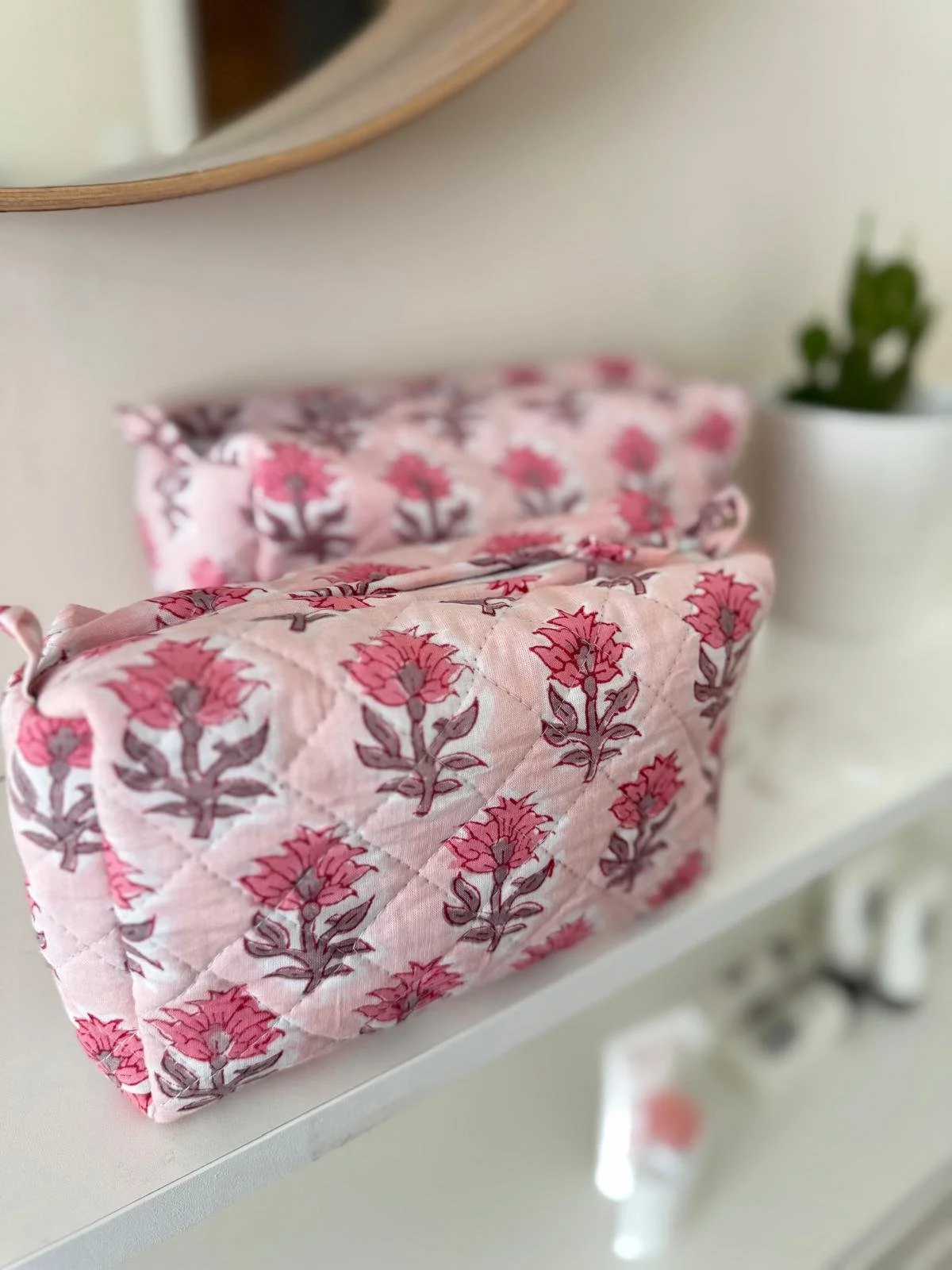 A medium and small block print pink floral wash bag with a quilted cotton texture resting on a white shelf