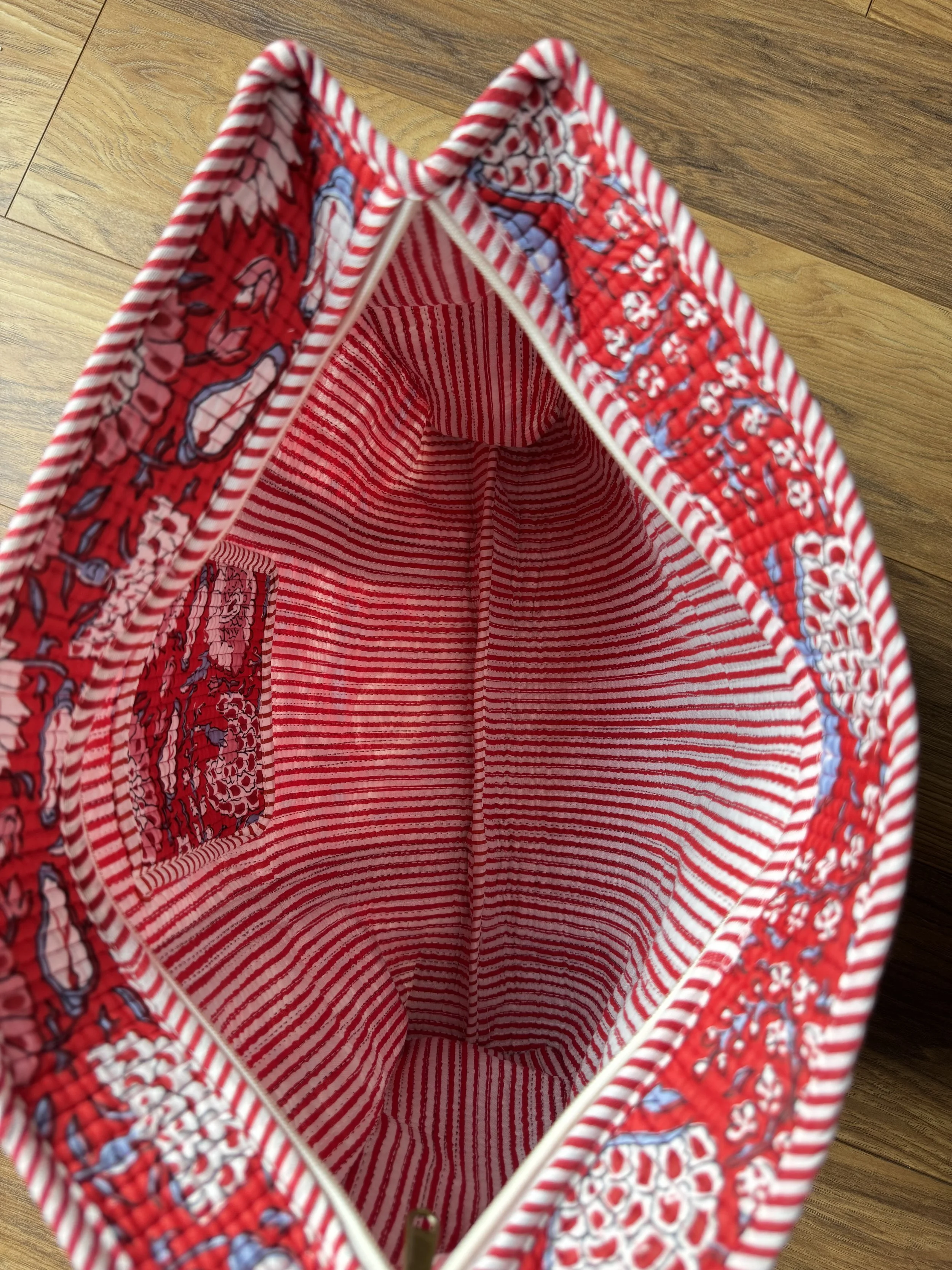 Open zipper revealing striped red and white lining and floral print of inside pocket on a vibrant red quilted cotton shopper bag by jewelled Buddha