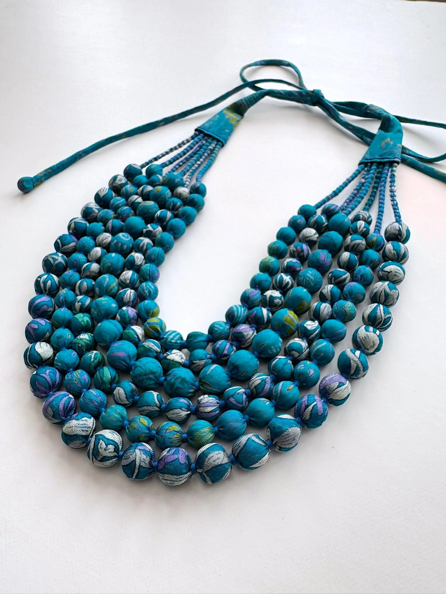 Close up of vibrant six strand sari bead necklace on a white background