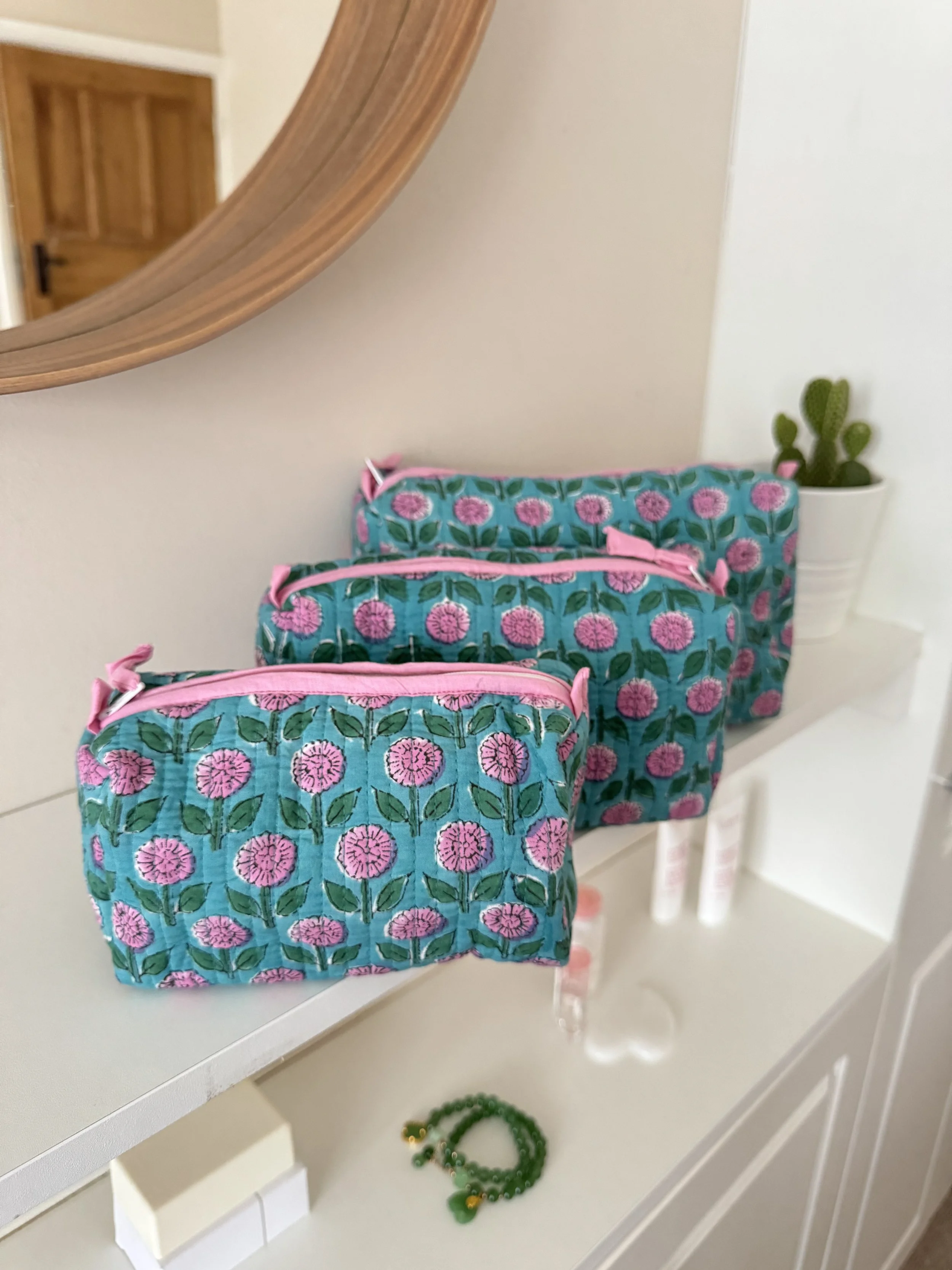 Set of three hand block printed make up and toiletry pouches resting on a white shelf