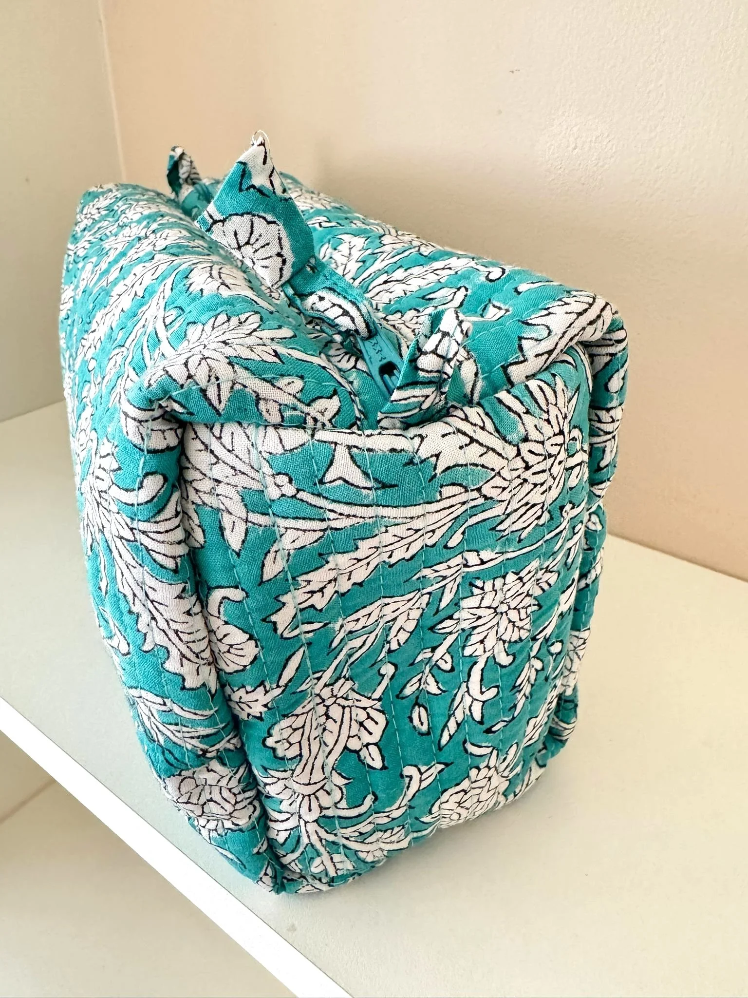 Close up of floral make up bag in turquoise with a leafy botanical print