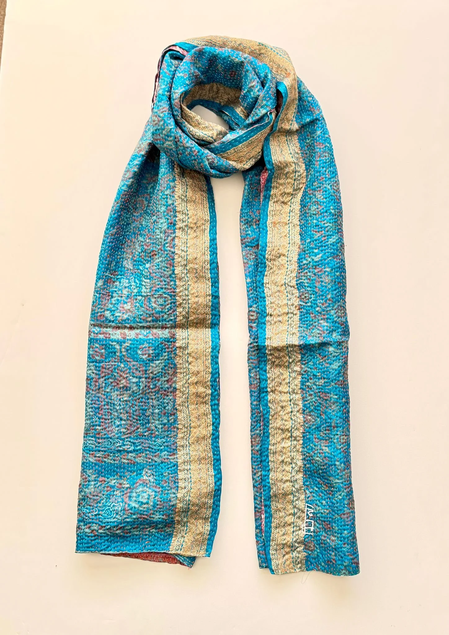 A blue and gold patterned silk scarf draped elegantly over a mannequin against a peach background