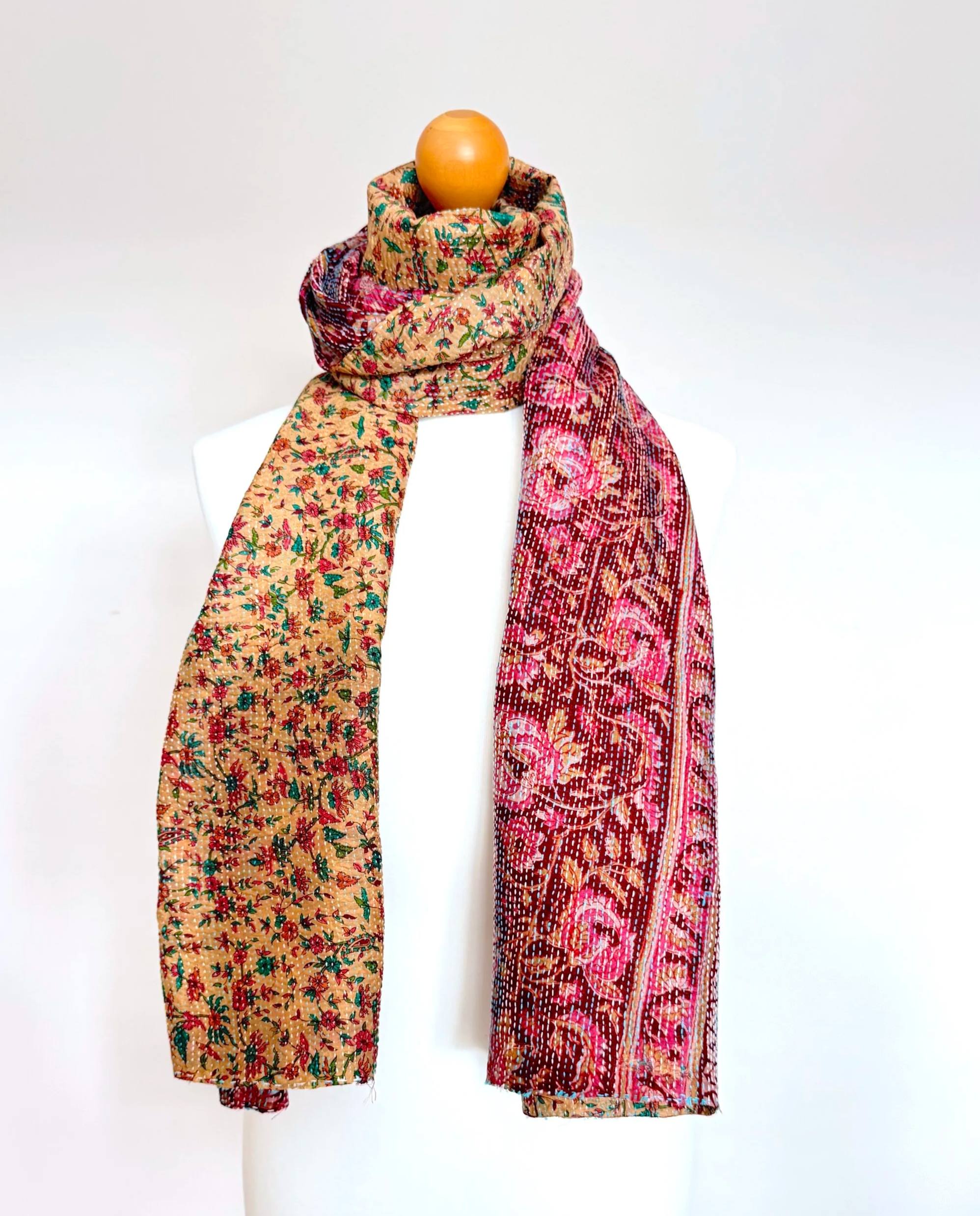 A vibrant scarf with a floral pattern in red and green draped over a mannequin in a neutral background. The scarf conveys a warm, elegant feel.